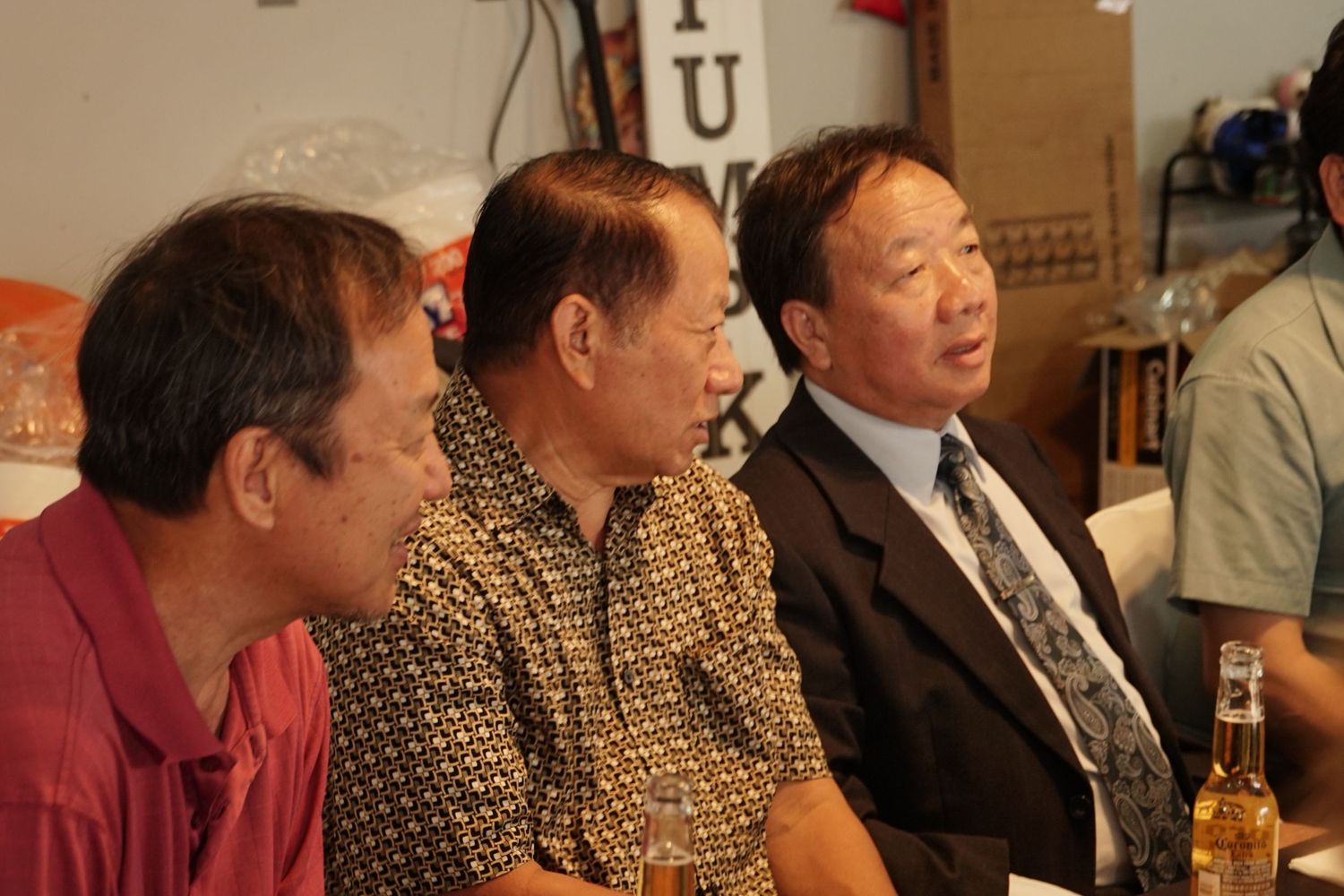 Three Asian men sitting together at a table in conversation, with drinks visible in the background.