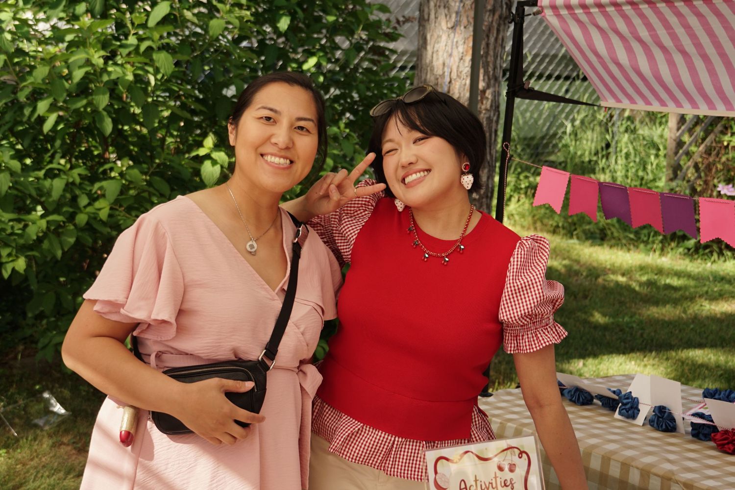 Two smiling women pose together outdoors at a garden party, one in pink and one in red.