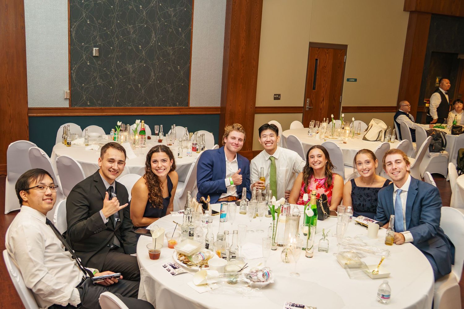 Group of young adults smiling at a round table during a formal banquet event in an elegant ballroom.