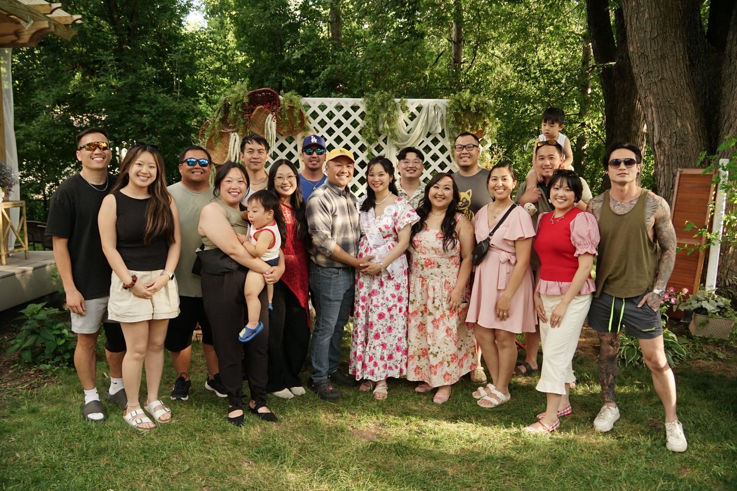 A large group of smiling family and friends posing together outdoors in a lush green garden during a summer gathering.