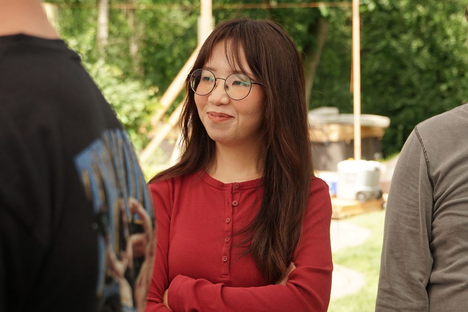 A young Asian woman with glasses and red top smiling outdoors at a social event.