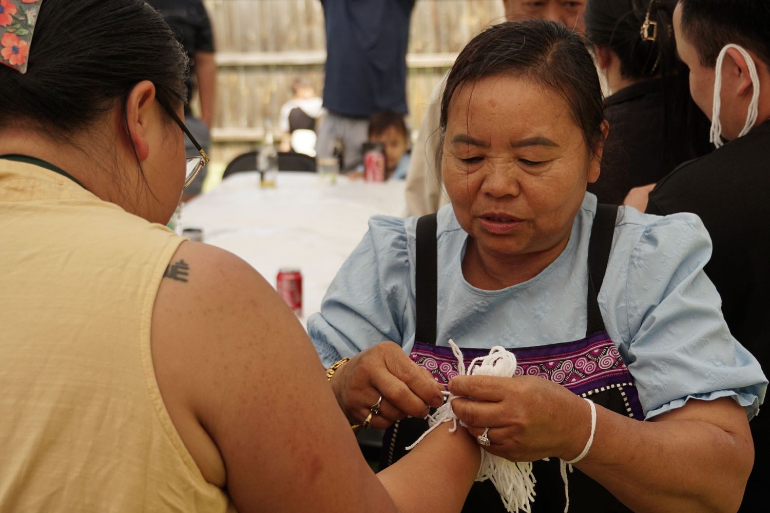 A woman carefully applies traditional beadwork to another persons arm at a cultural gathering or festival.