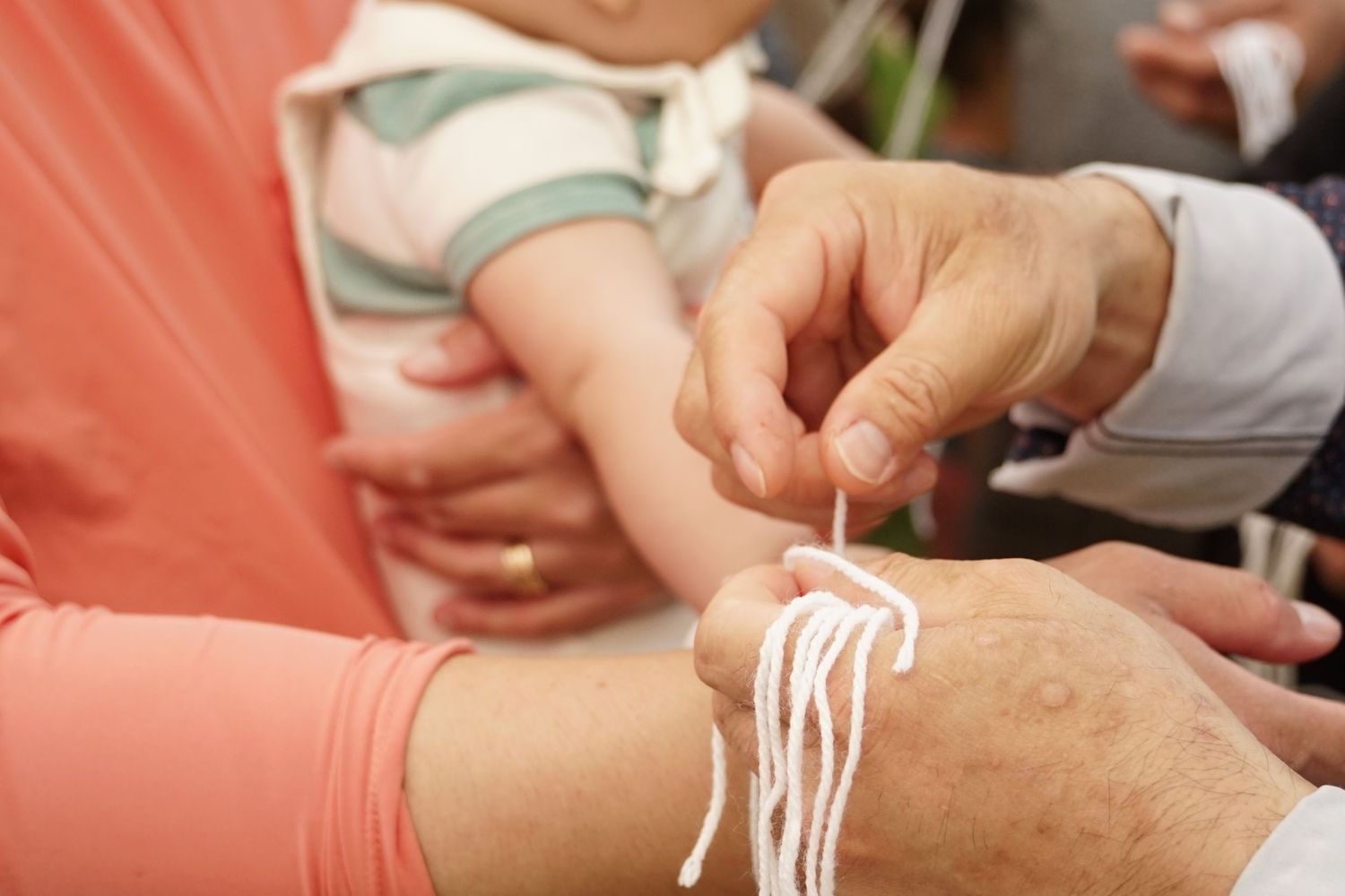 Adult tying white string bracelet on baby's wrist during a religious or cultural ceremony.