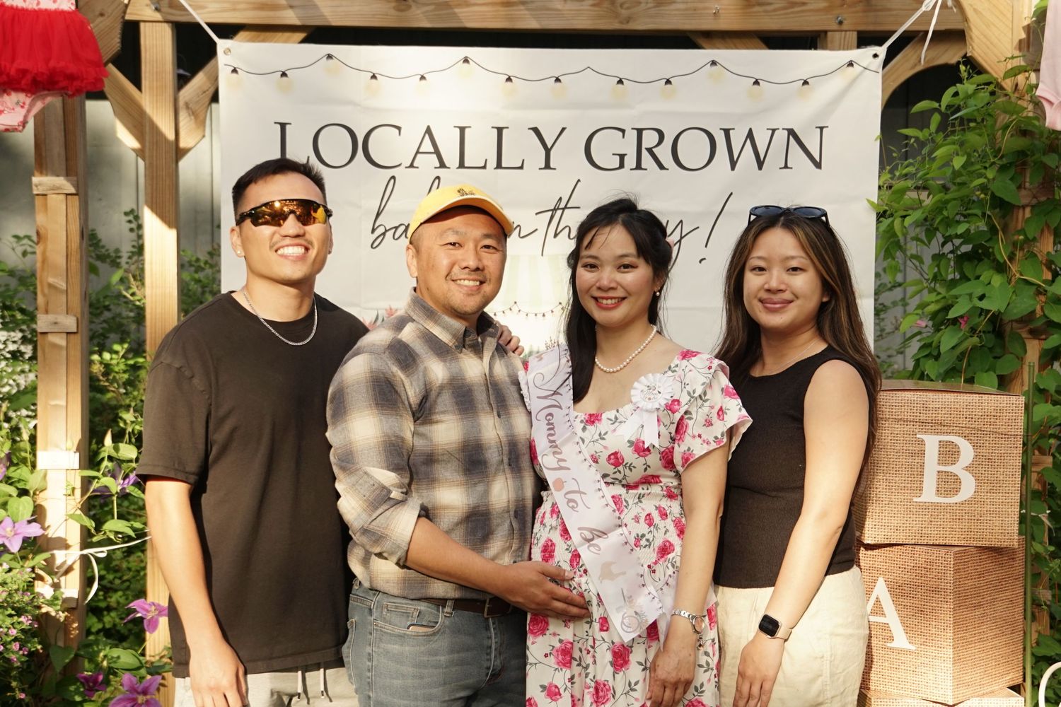 Four people smiling together at a Locally Grown baby shower celebration outdoors.