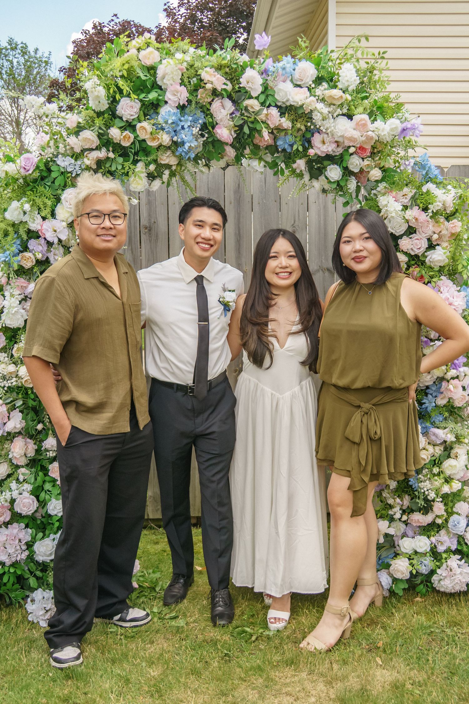 Family of four poses under lush floral arch at outdoor spring celebration event.