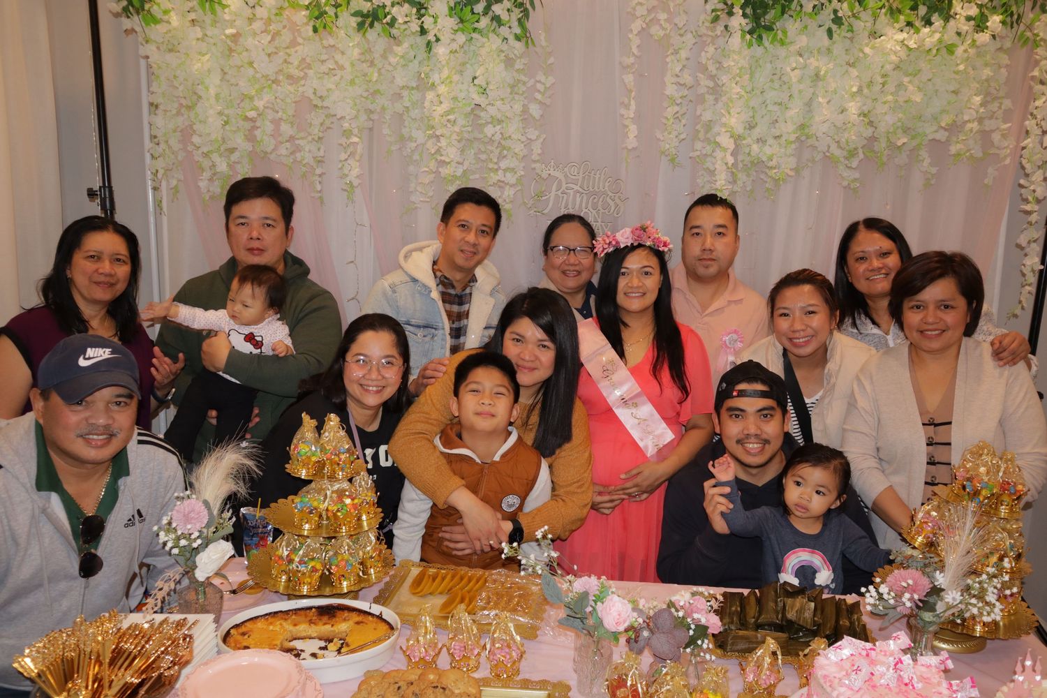 Large family group photo at festive baby shower celebration with golden decorations.
