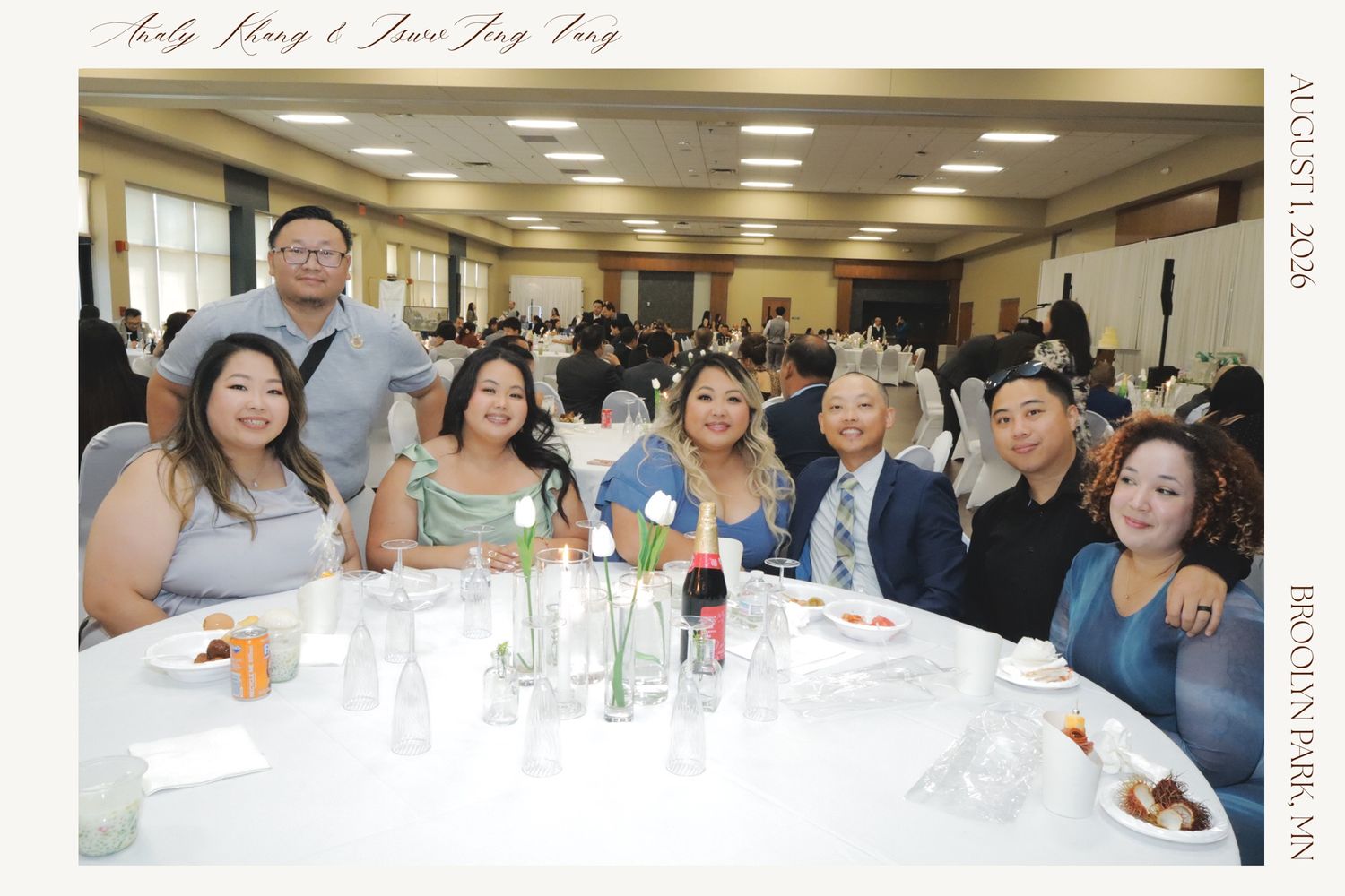 Group of friends smiling together at a formal banquet hall event, seated at a decorated table with bottles and glassware.
