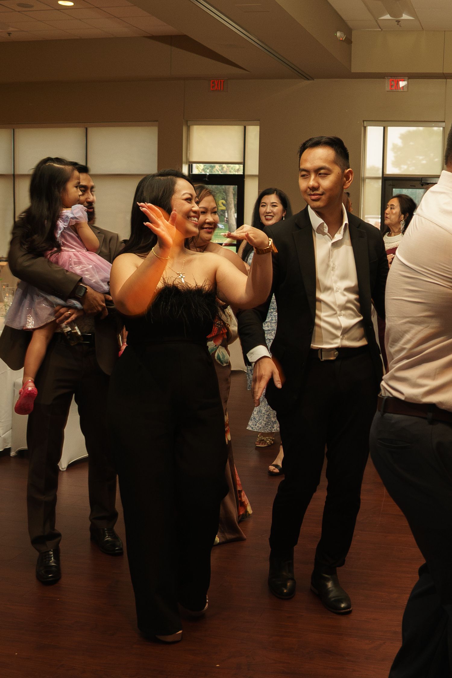 Guests dancing and socializing at an elegant indoor event, wearing formal black attire in a well-lit banquet hall.
