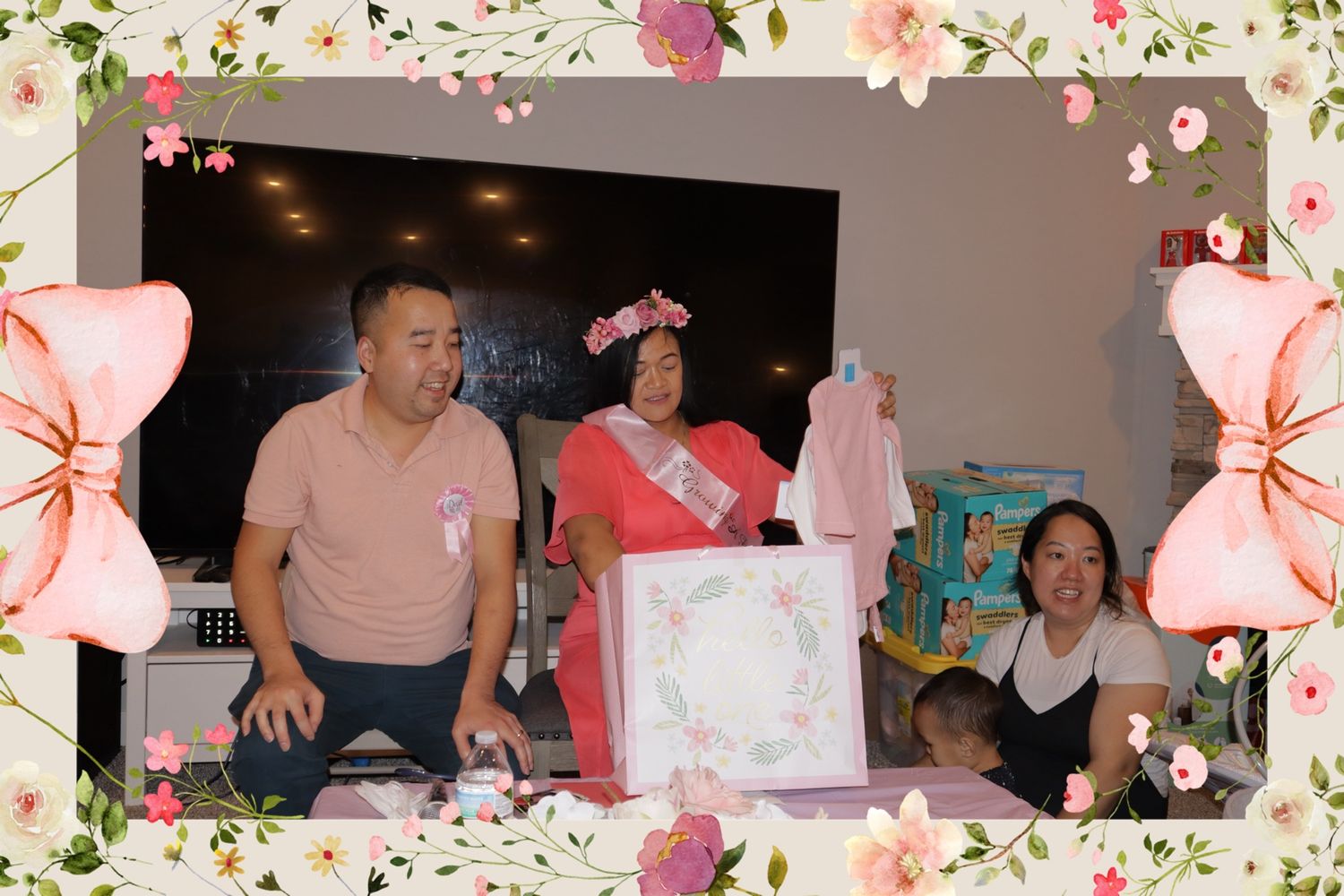 Family gathers around mom-to-be wearing sash and crown at floral-framed baby shower.
