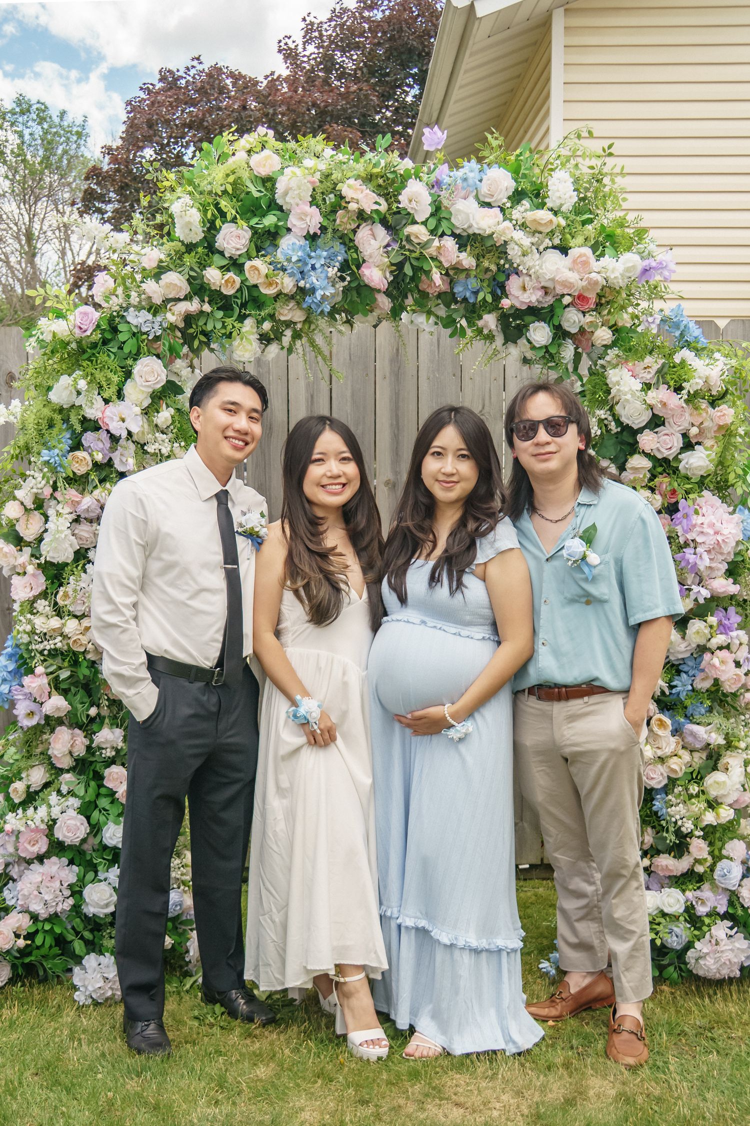 Pregnant woman in blue dress poses with three friends under floral arch at baby shower.