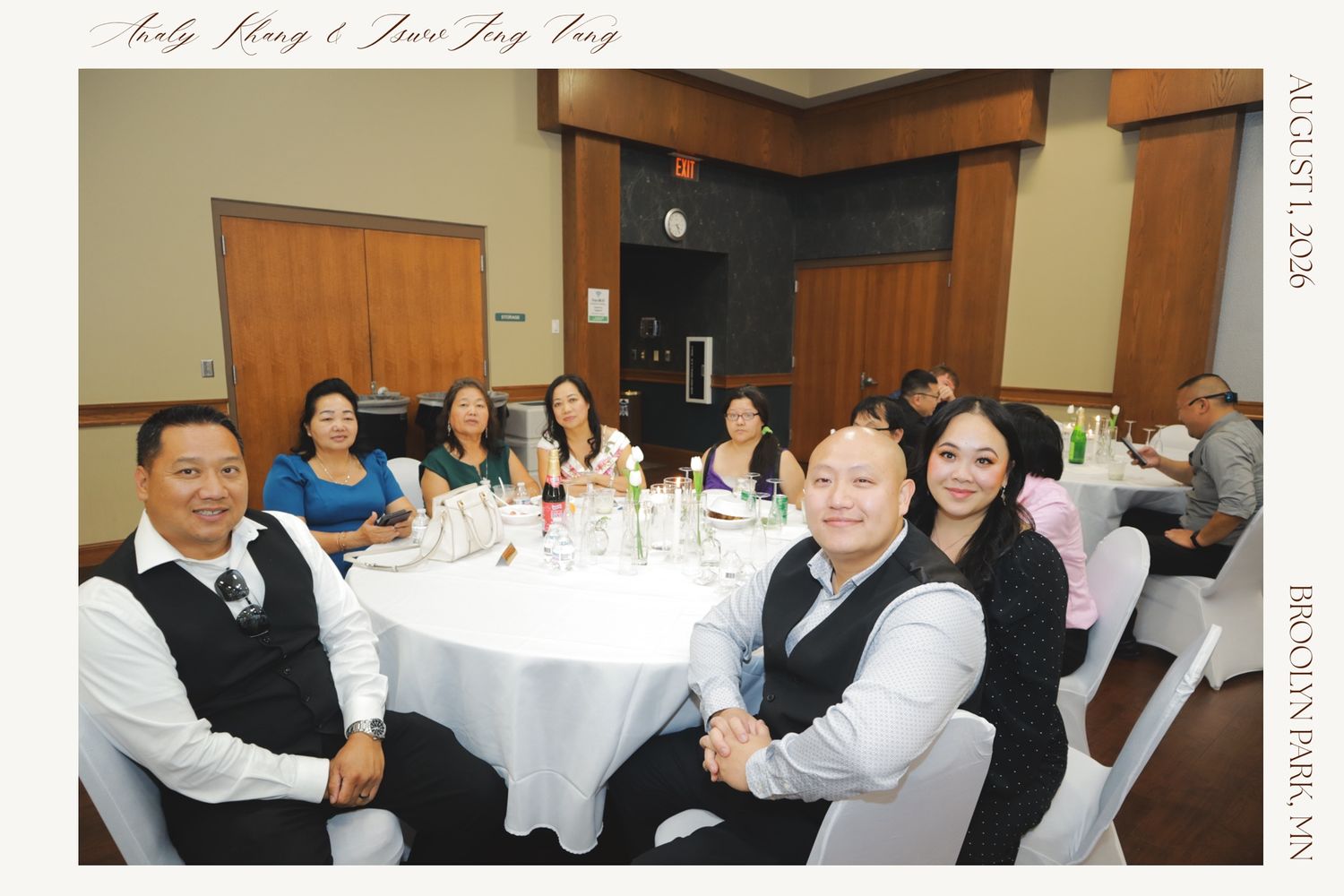 Group of guests smiling at a round table during a wedding reception banquet in a decorated hall.