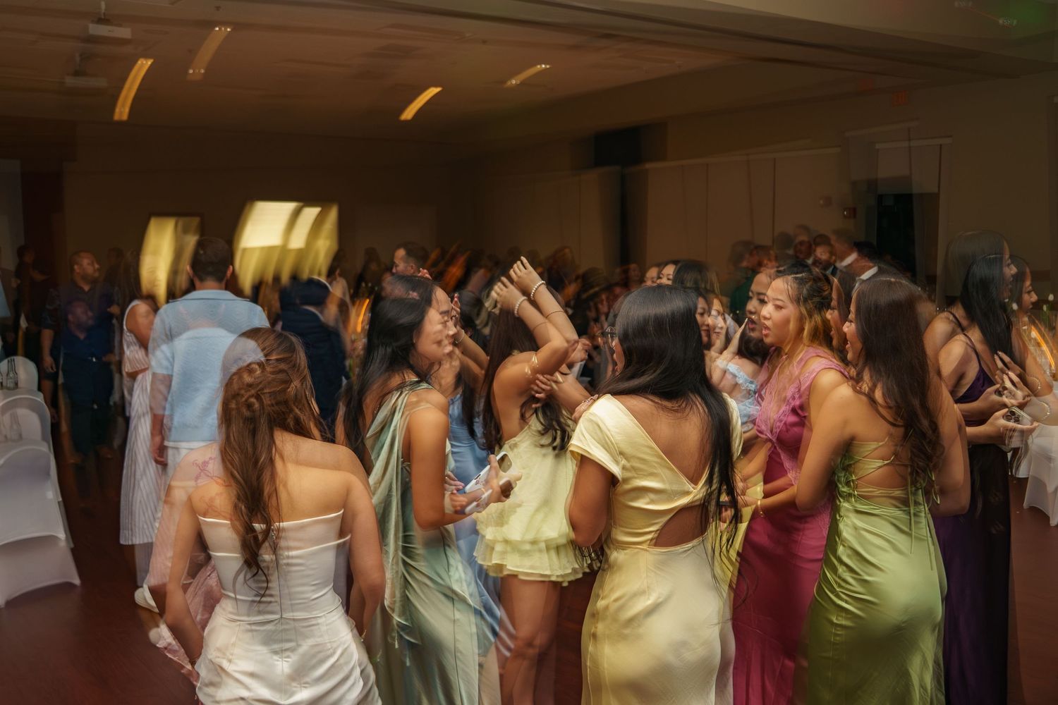 Guests in colorful formal gowns dancing at an elegant indoor celebration or wedding reception.