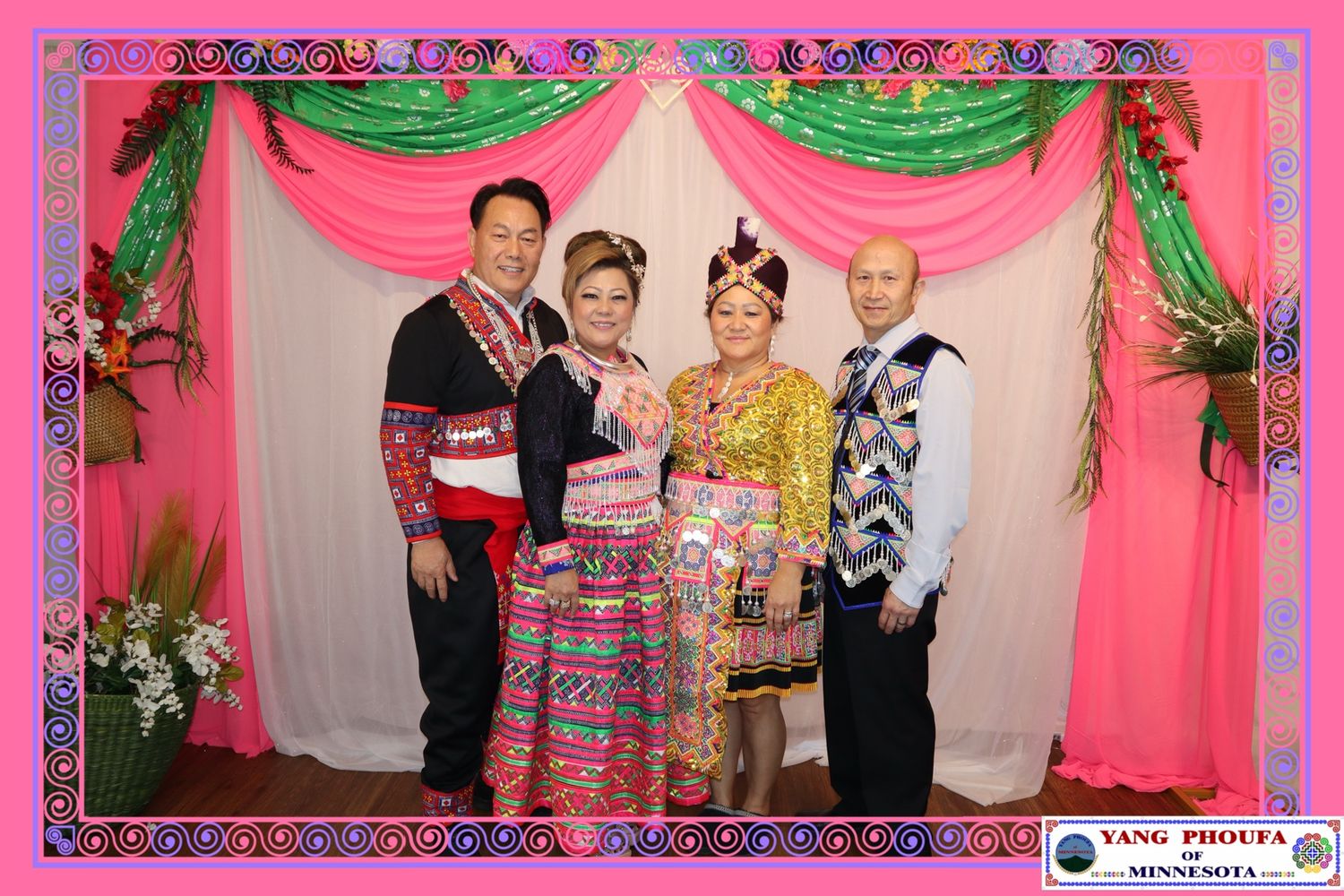 Four people in colorful traditional Hmong clothing pose together at a festive New Year celebration.