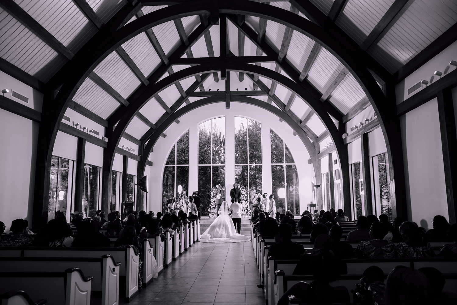 Black and white photo of a wedding ceremony inside a chapel with vaulted wooden ceilings.