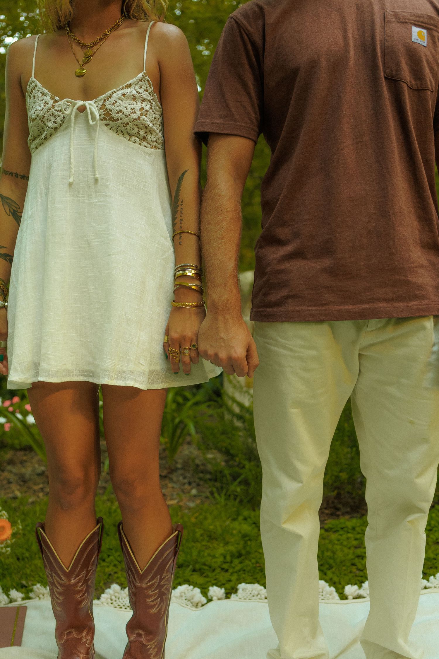 Row of brown cowboy boots worn with white and brown clothing against green outdoor background.