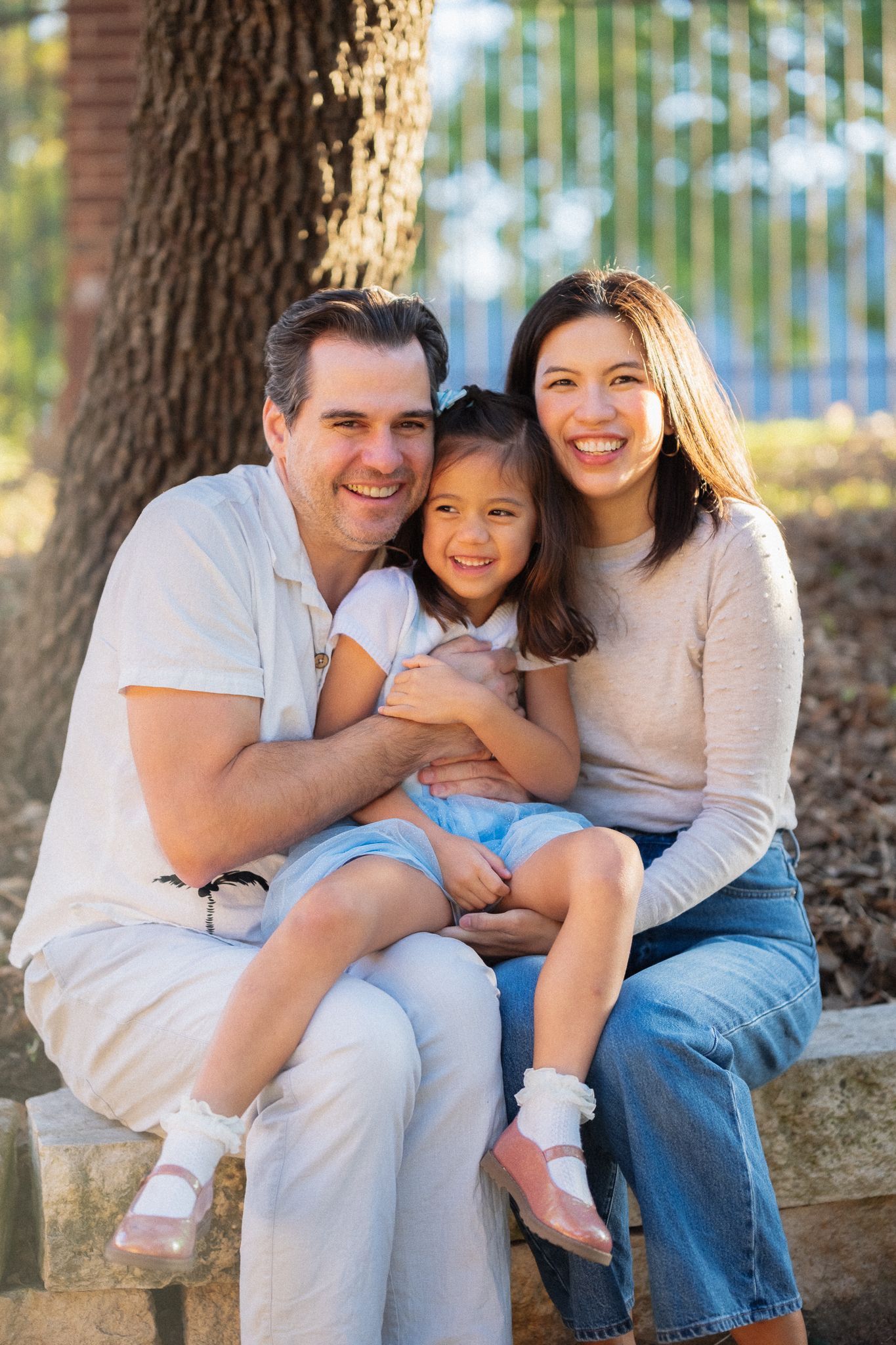 Family sitting together on stone steps under trees sharing intimate moments during an outdoor photo session.