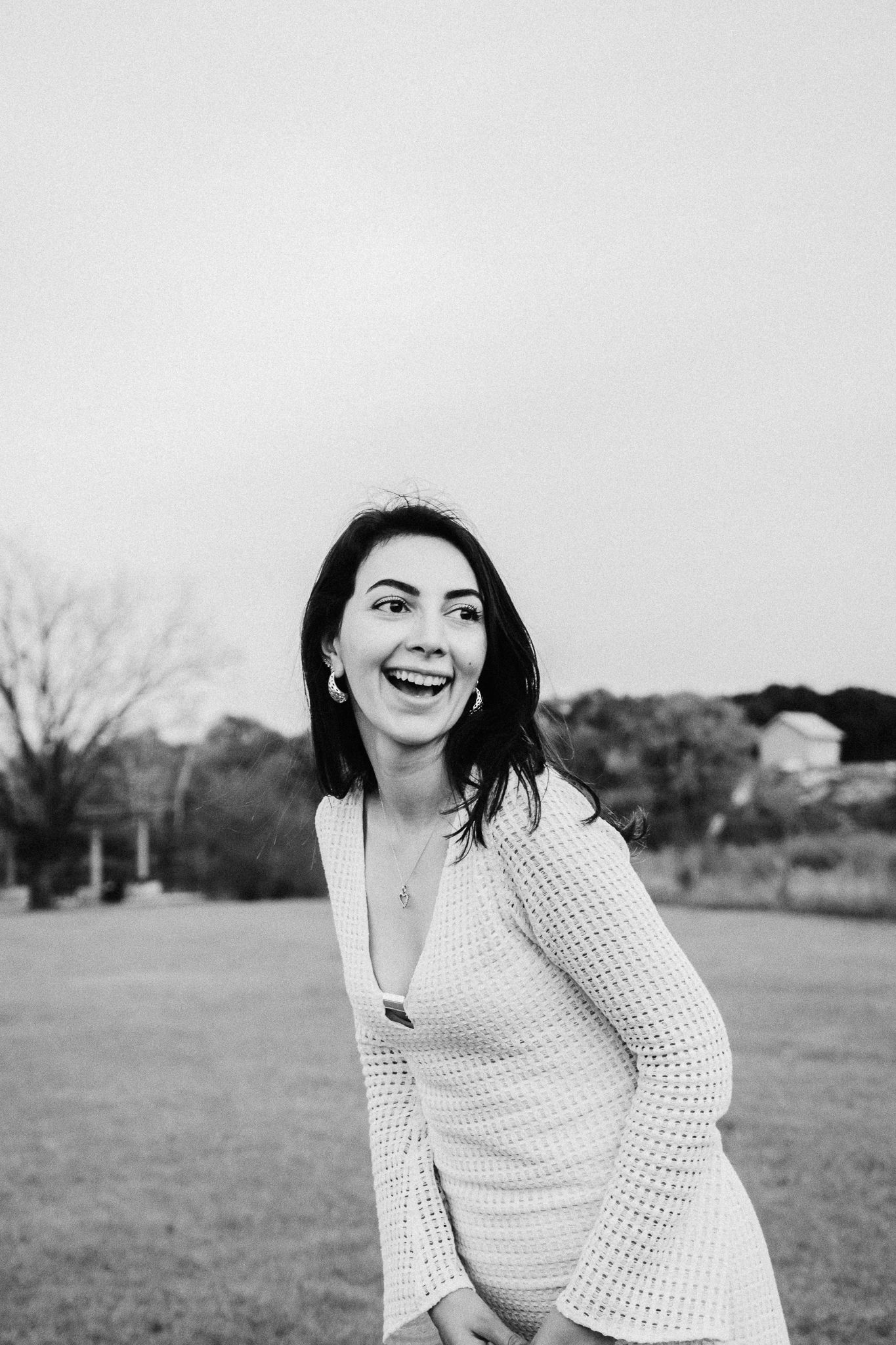 A candid black and white portrait shows a person in a white knit sweater laughing joyfully outdoors.
