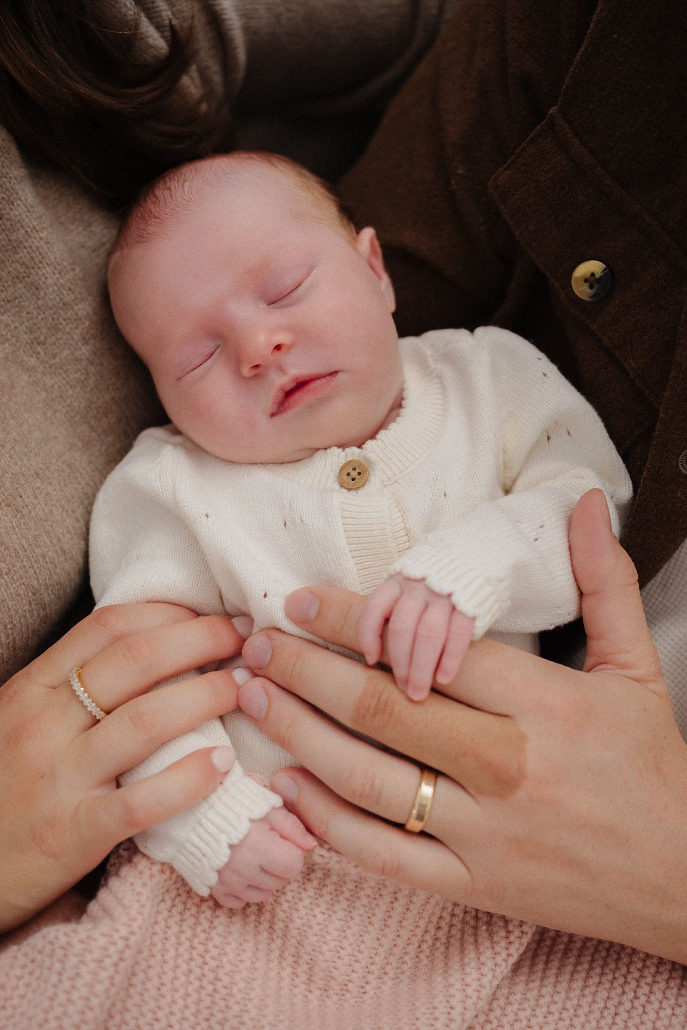 A sleeping newborn baby wearing a white knit sweater is cradled in someone's arms.