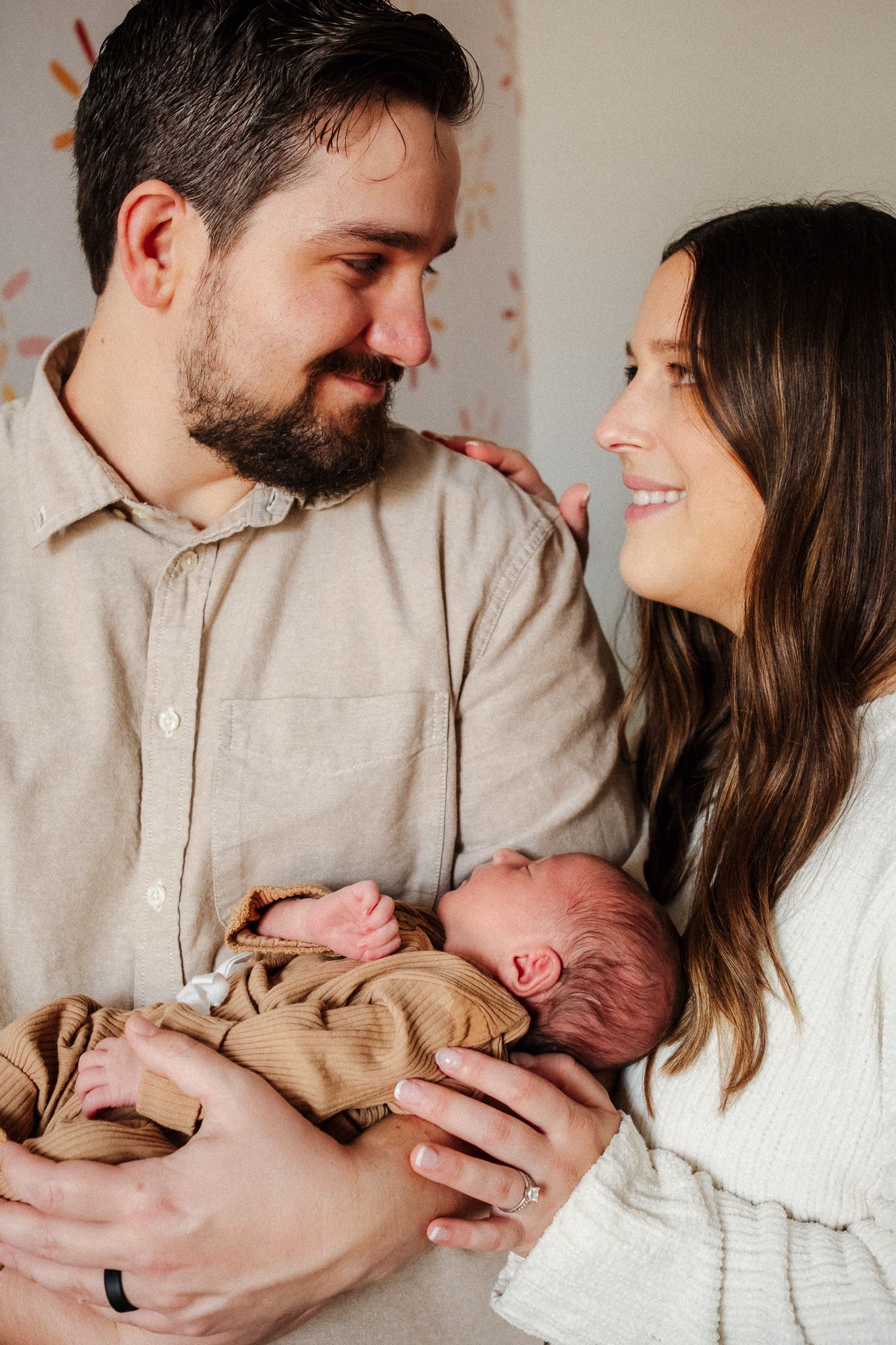 A loving family moment captured in a series of tender interactions with their newborn baby against a neutral backdrop.