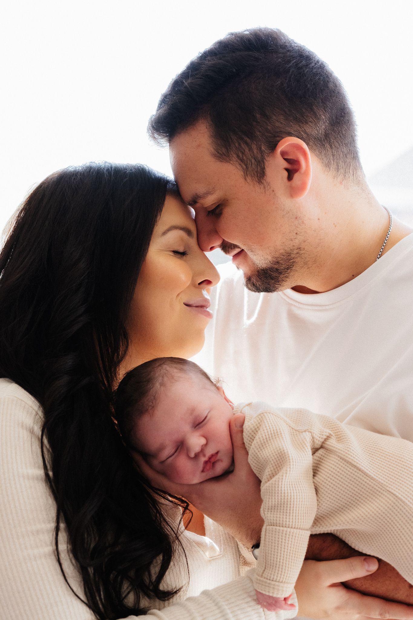 A touching family moment as parents share a gentle embrace while holding their sleeping newborn.