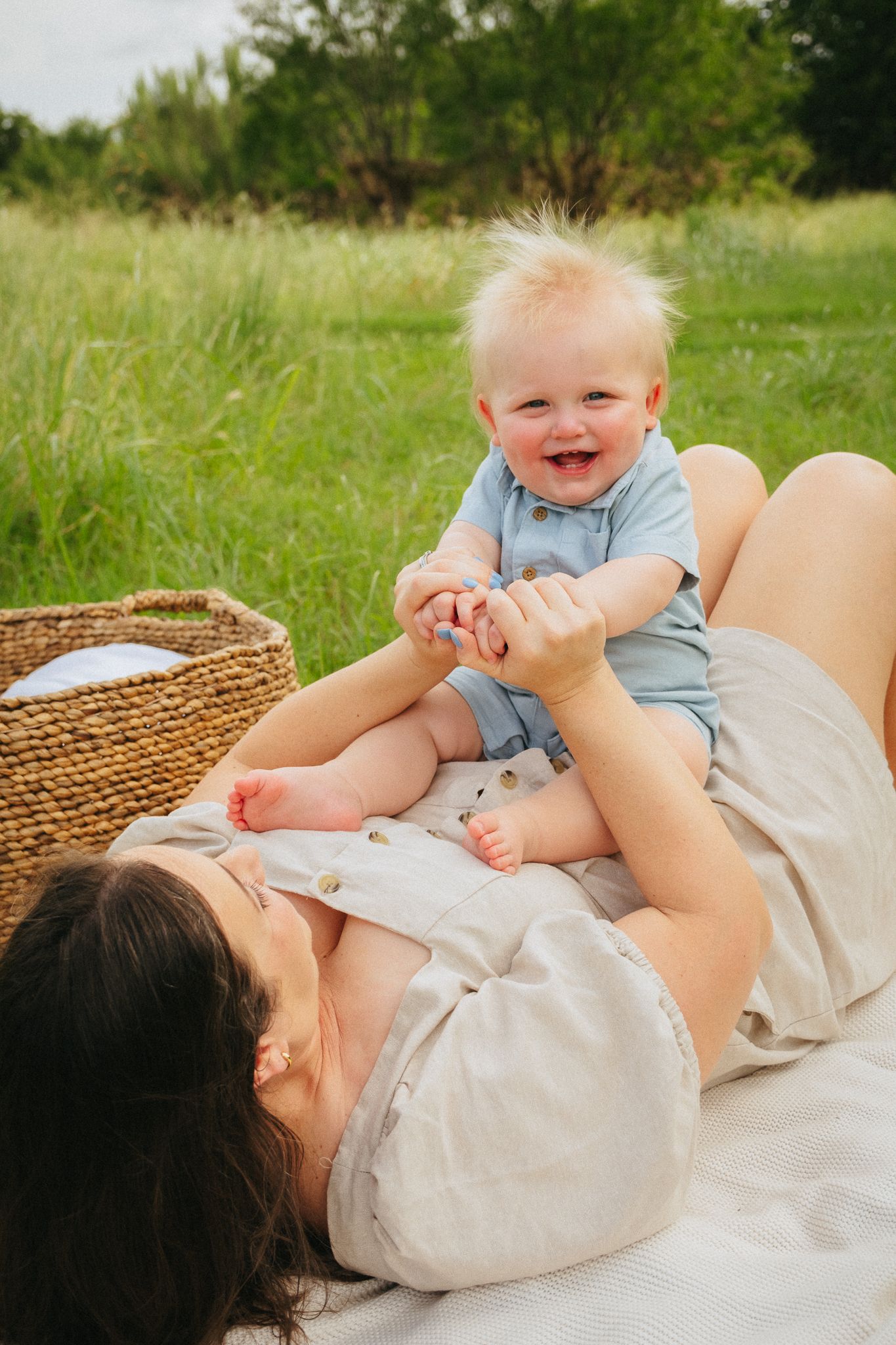 A joyful moment captured on a blanket in a grassy field with light and natural surroundings.