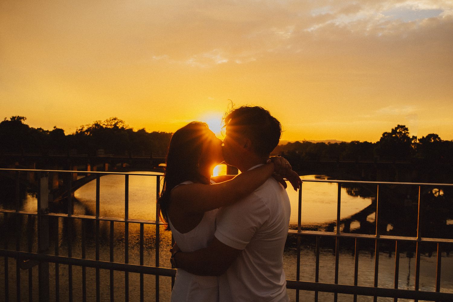Silhouettes of people watching a vibrant orange sunset over a lake from a viewing deck.