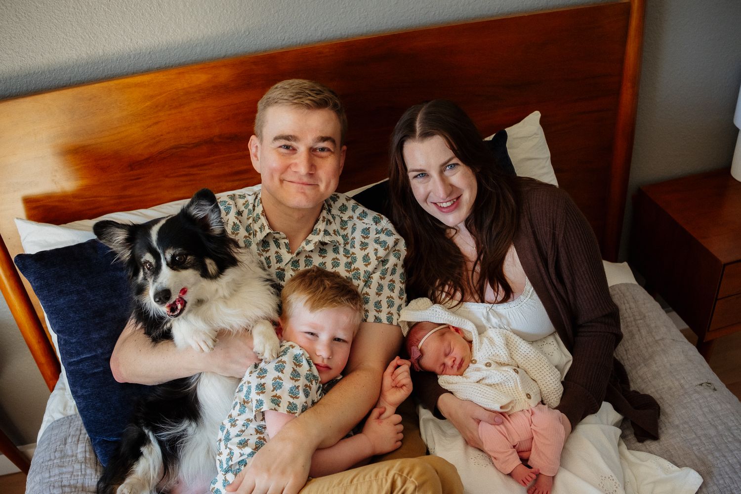 Family portrait on bed with parents, two children, and border collie dog celebrating new baby arrival.