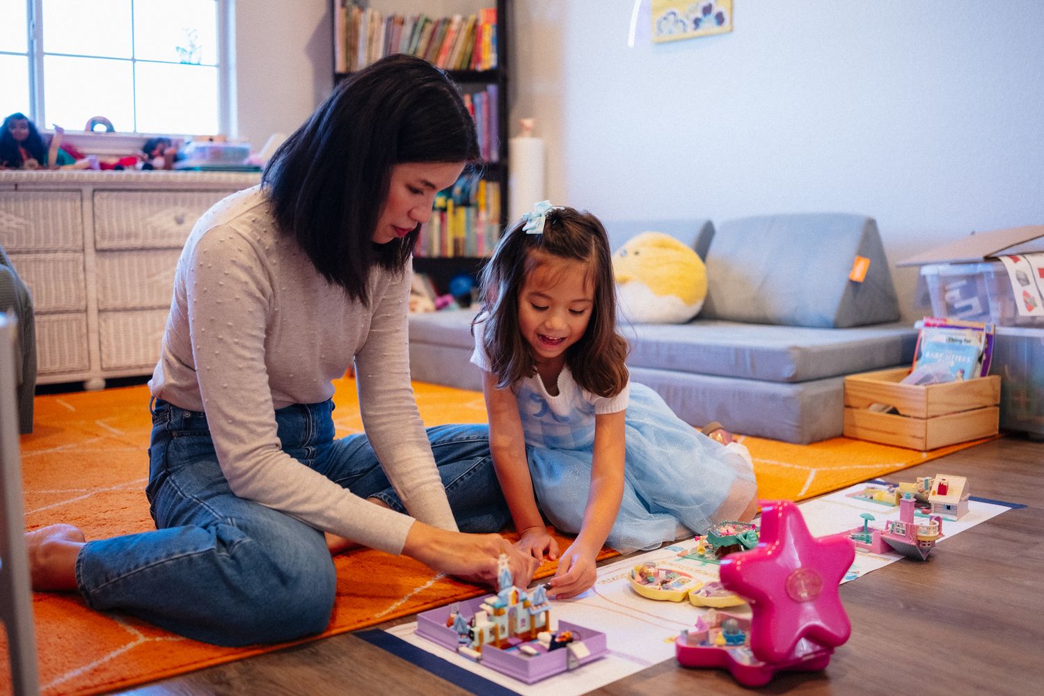 Two people sit on a carpeted floor playing with colorful building blocks and toys in a bright room.