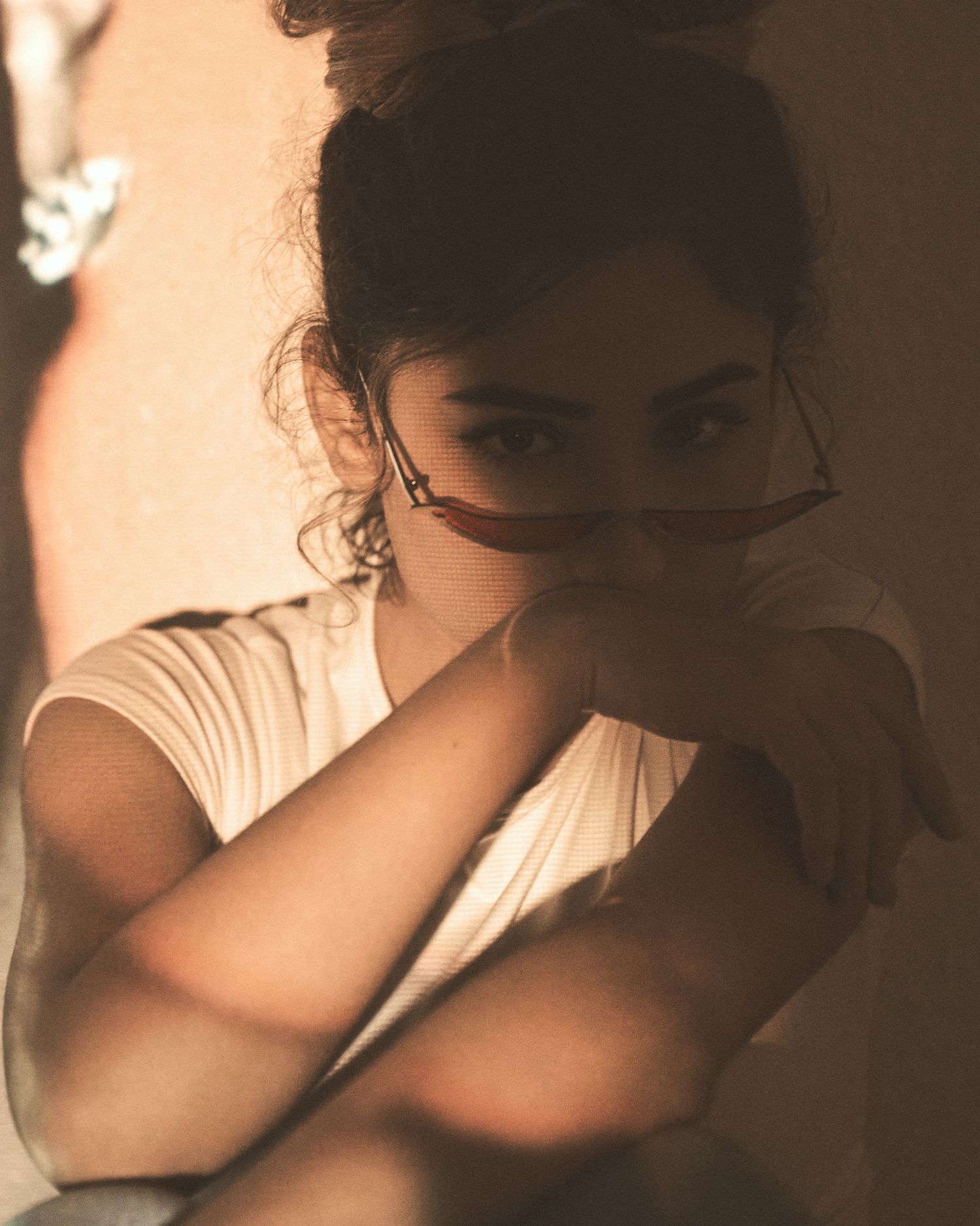 A sepia-toned portrait photograph of someone in a white shirt with their arms crossed and shadows creating a moody aesthetic.