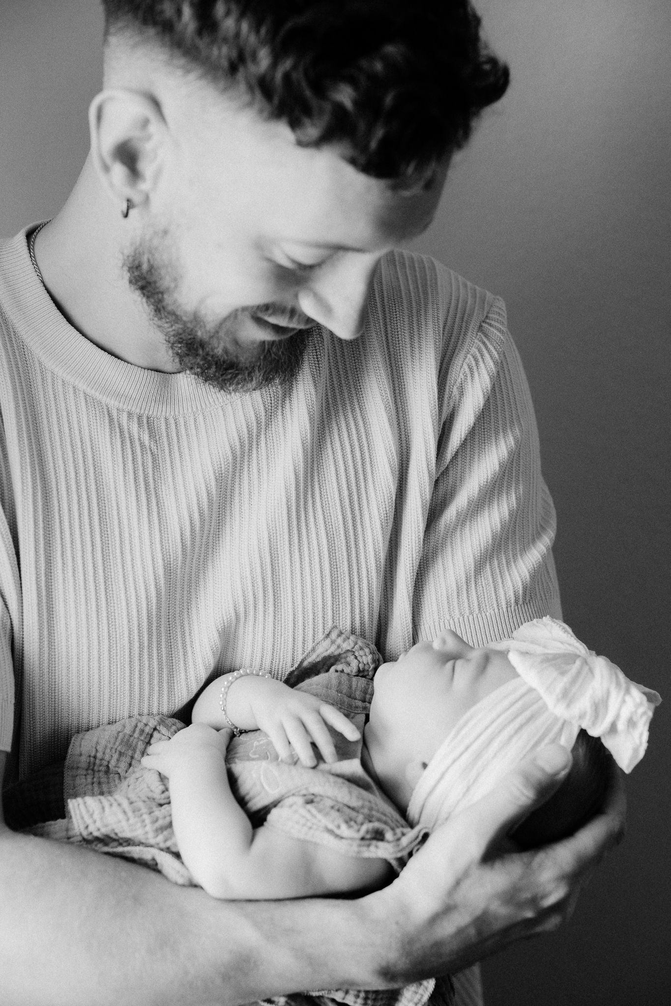 Black and white photo of a bearded father tenderly cradling his newborn baby in his arms.