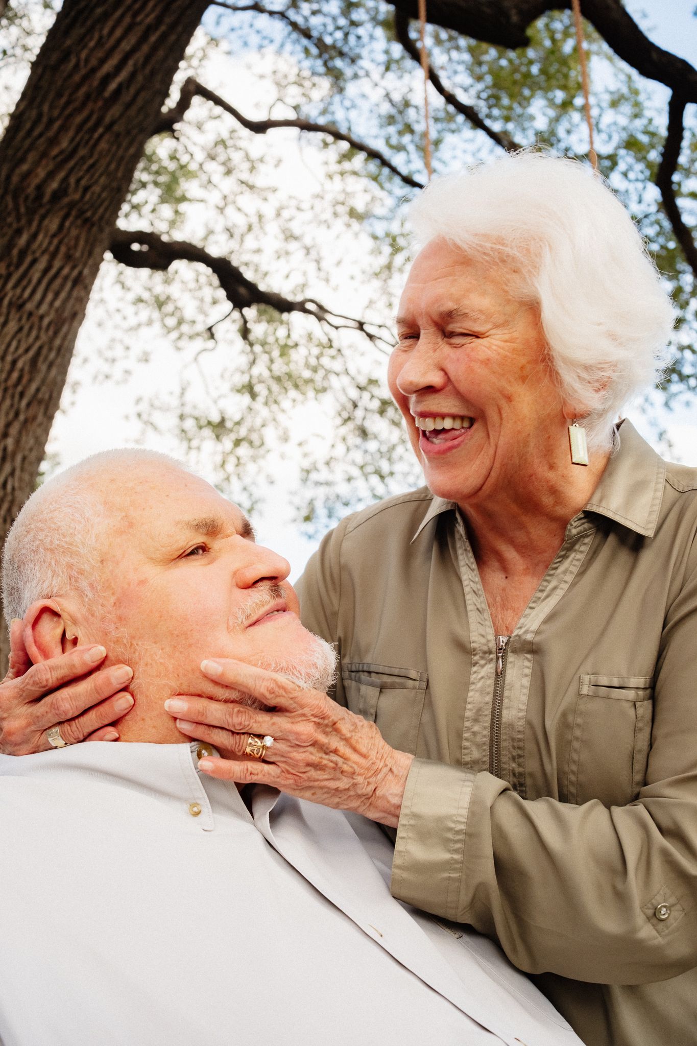 Two elderly women sharing an affectionate moment outdoors under a tree.