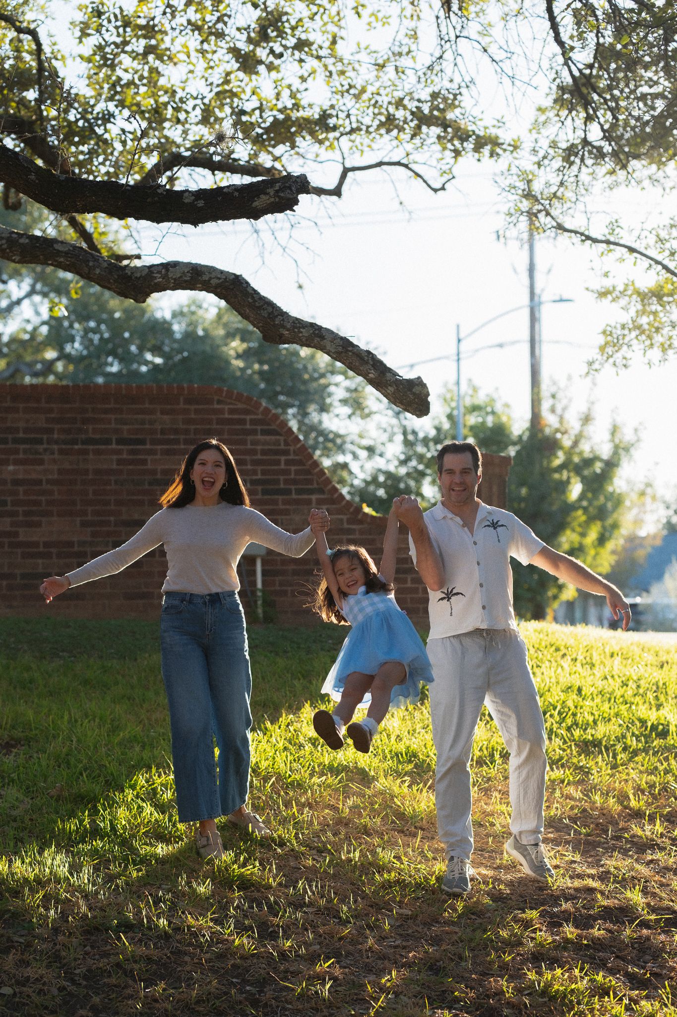 Couple dancing and twirling together on a grassy hillside during golden hour with trees in the background.