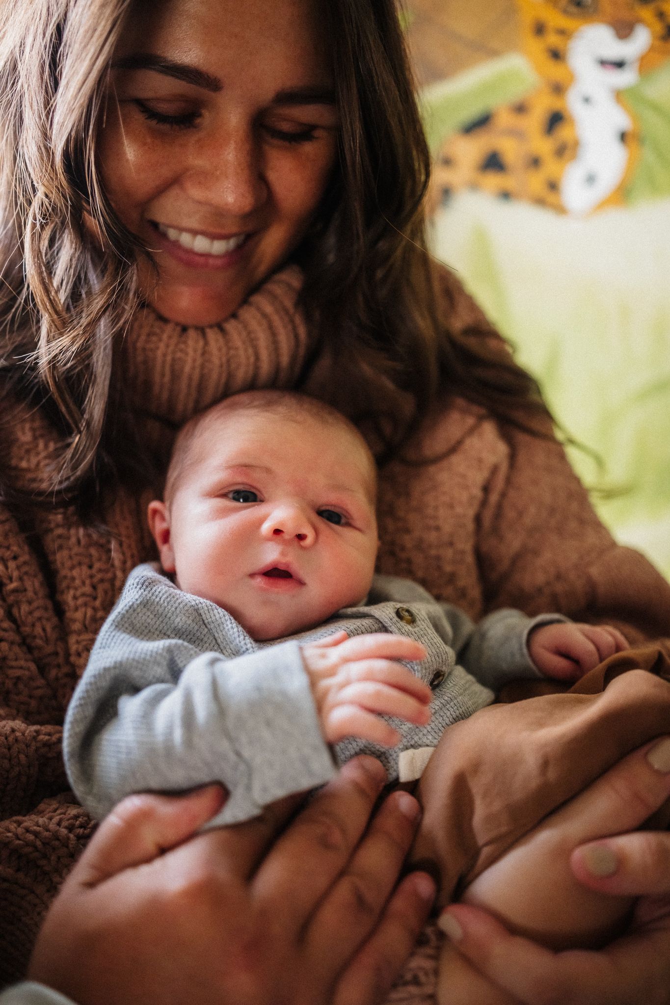 Tender moment between parent and baby in cozy brown sweater against yellow background.