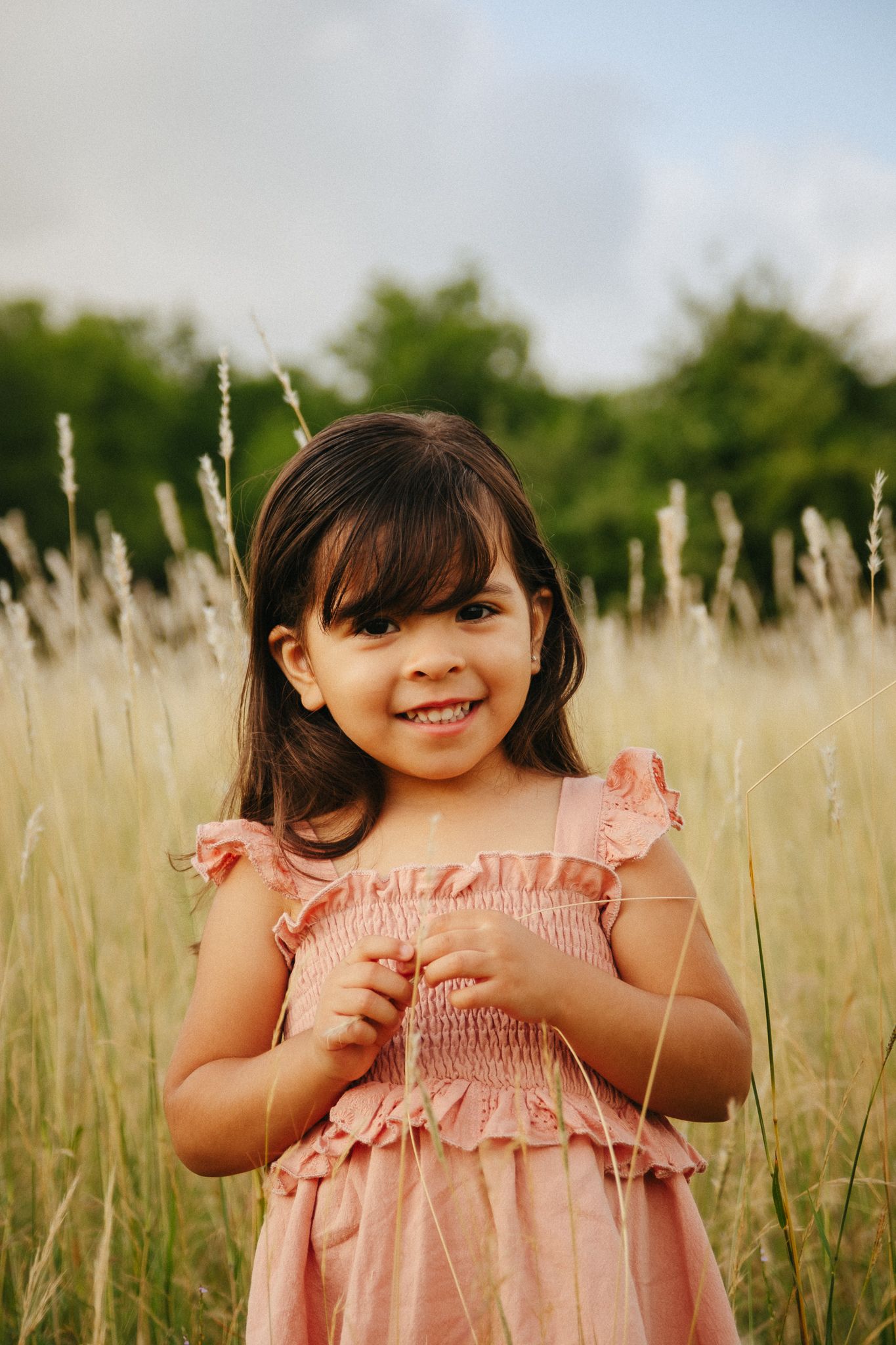 A child wearing a pink ruffled dress stands in a golden wheat field during golden hour.