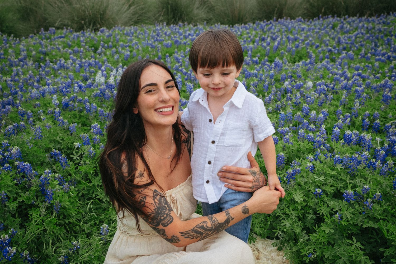 Two people smile together while sitting in a vibrant field of blooming bluebonnets during spring.