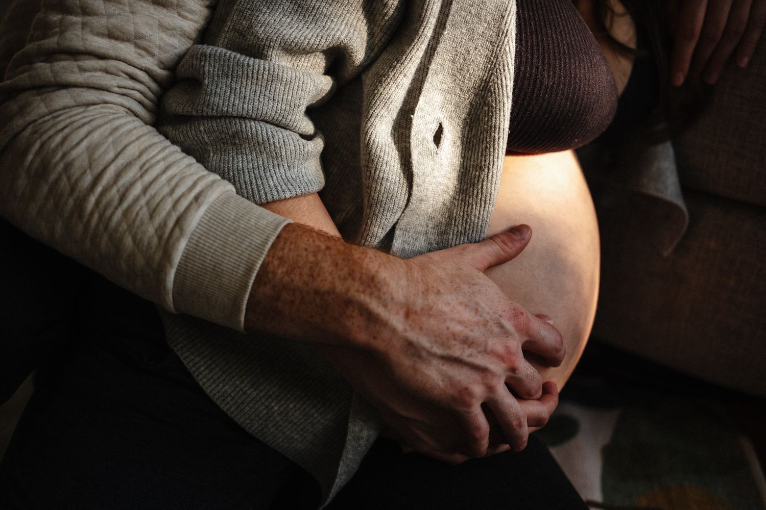 Close-up view of hands gently resting on a pregnant belly in soft natural lighting.