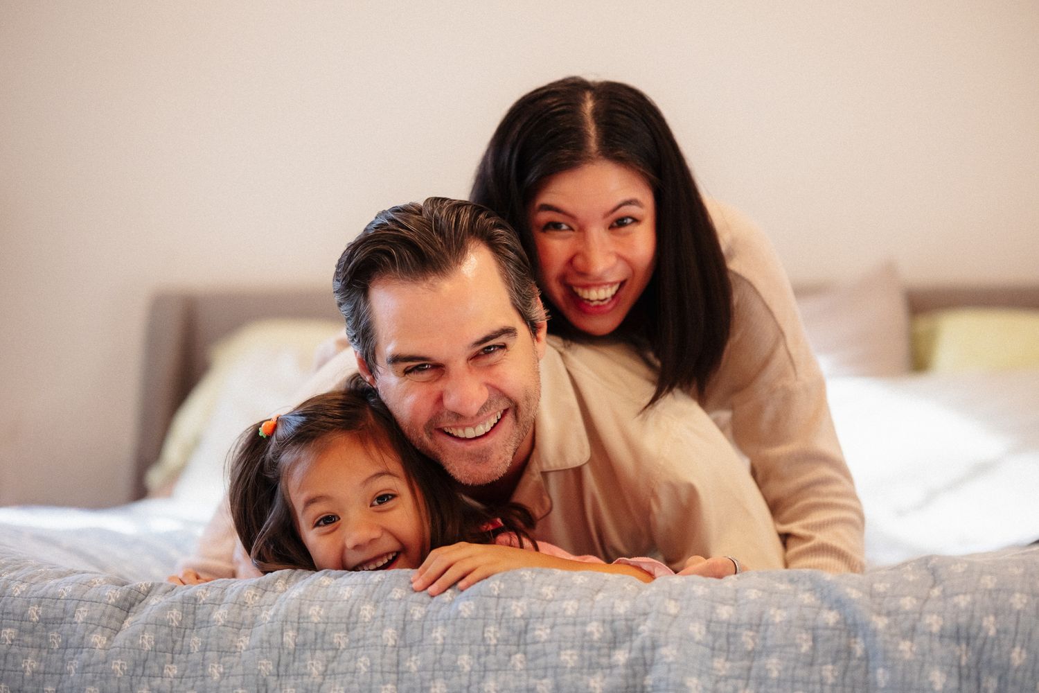 Happy family sharing tender moments while lying together on a cozy bed in warm lighting.