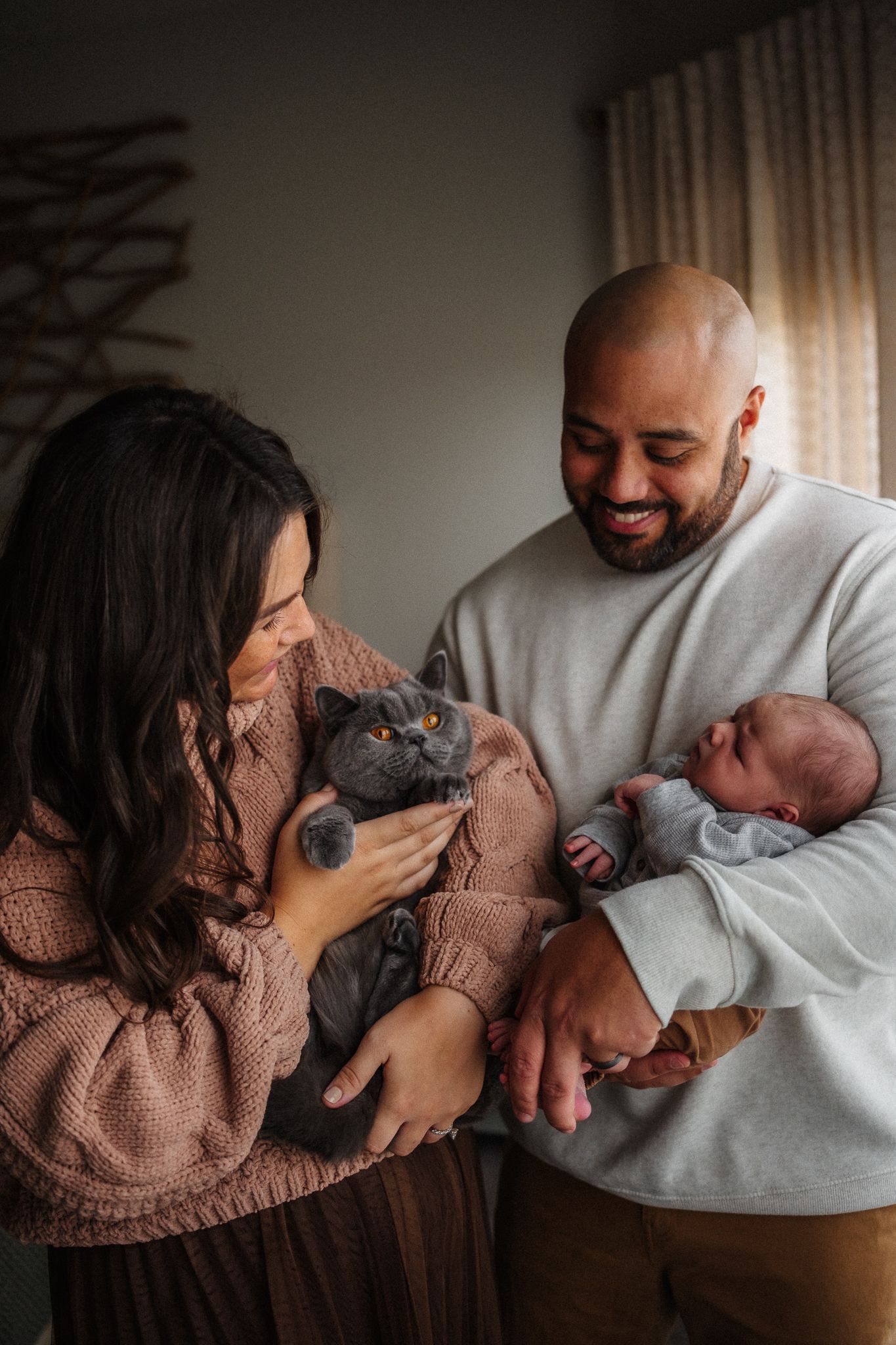 A loving couple in cozy sweaters share tender moments with their small gray cat in a series of intimate indoor photos.