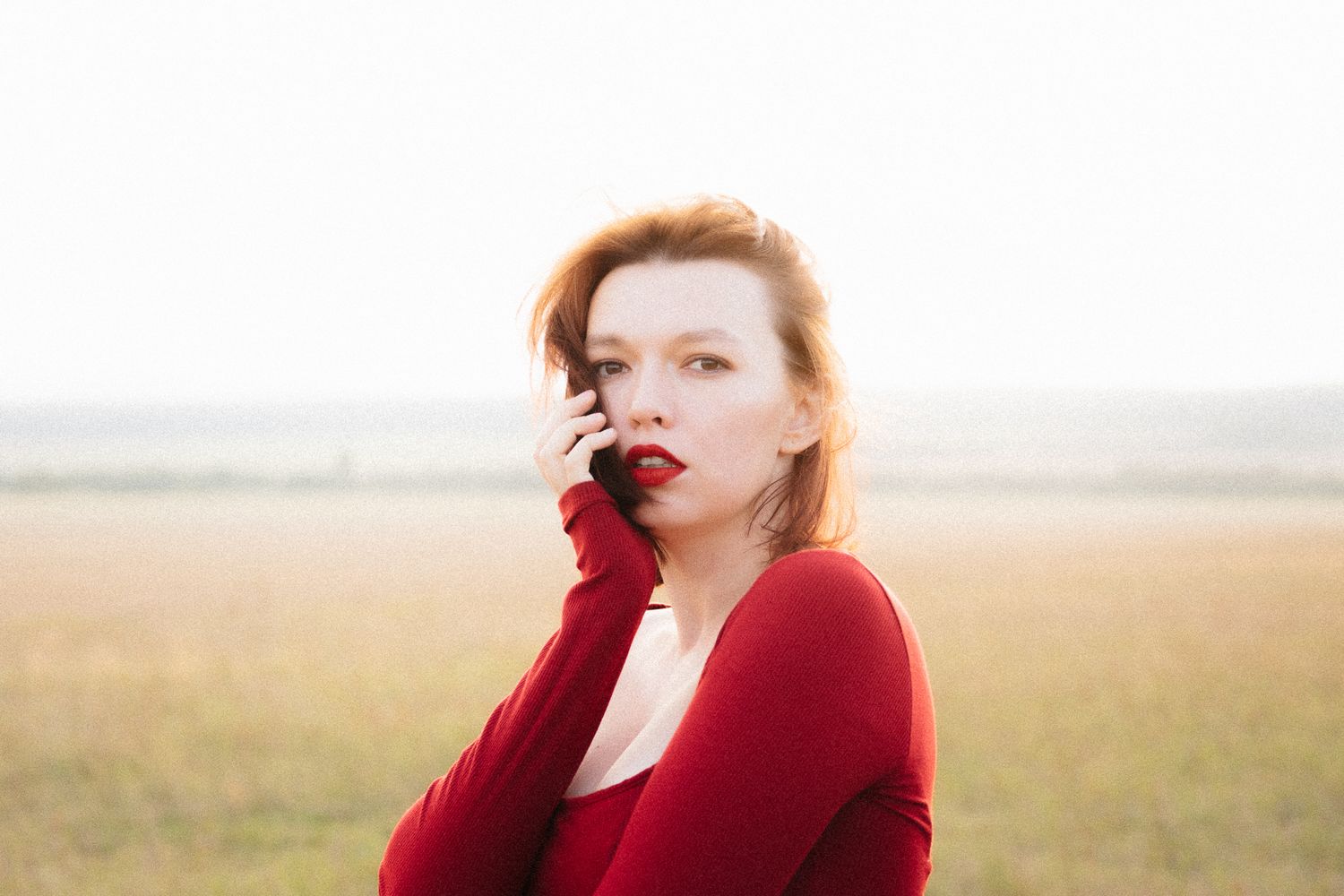 A person in a red dress stands dramatically in an open field during golden hour.