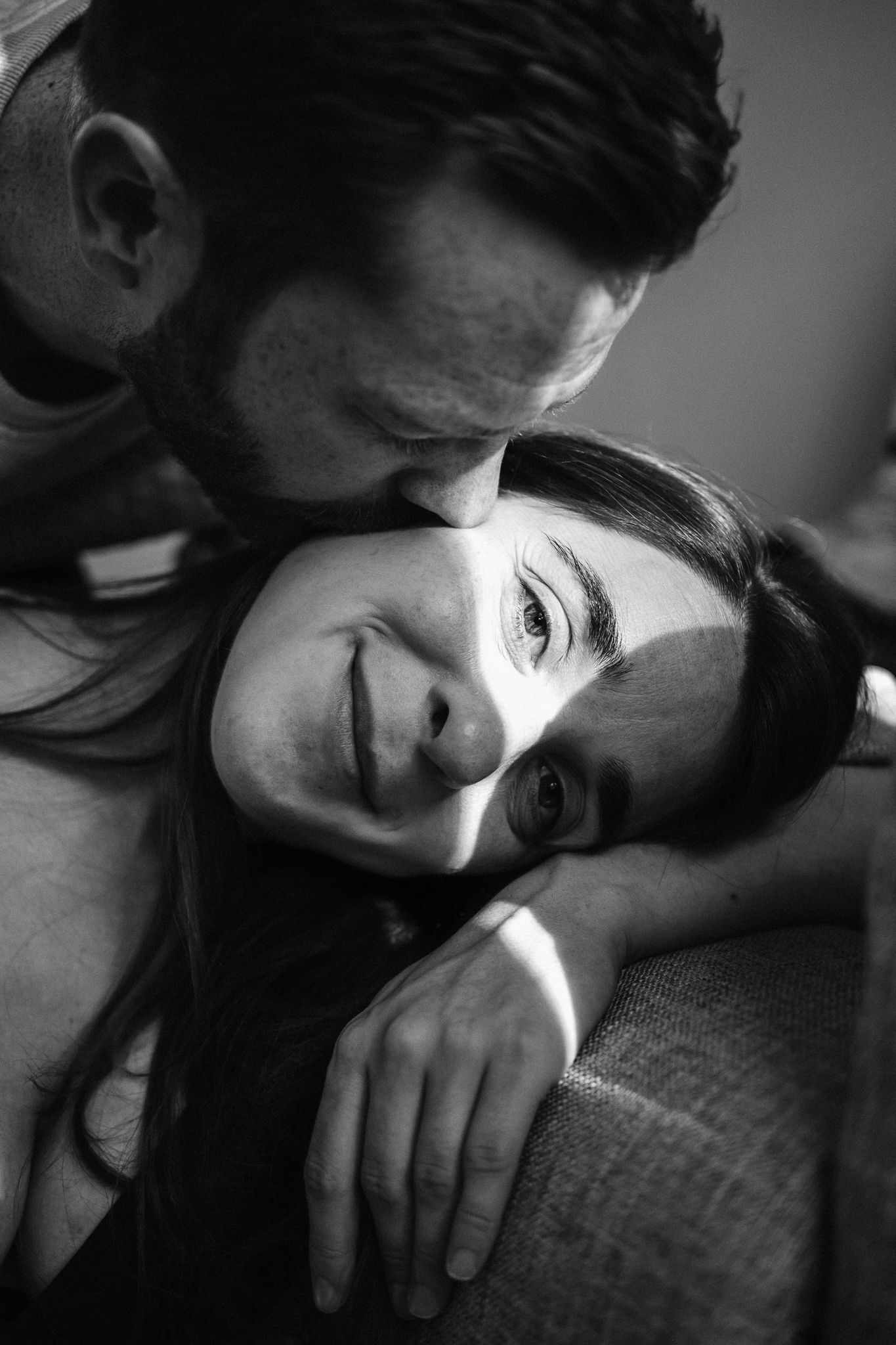 A tender black and white portrait of a couple sharing an intimate moment on a couch.