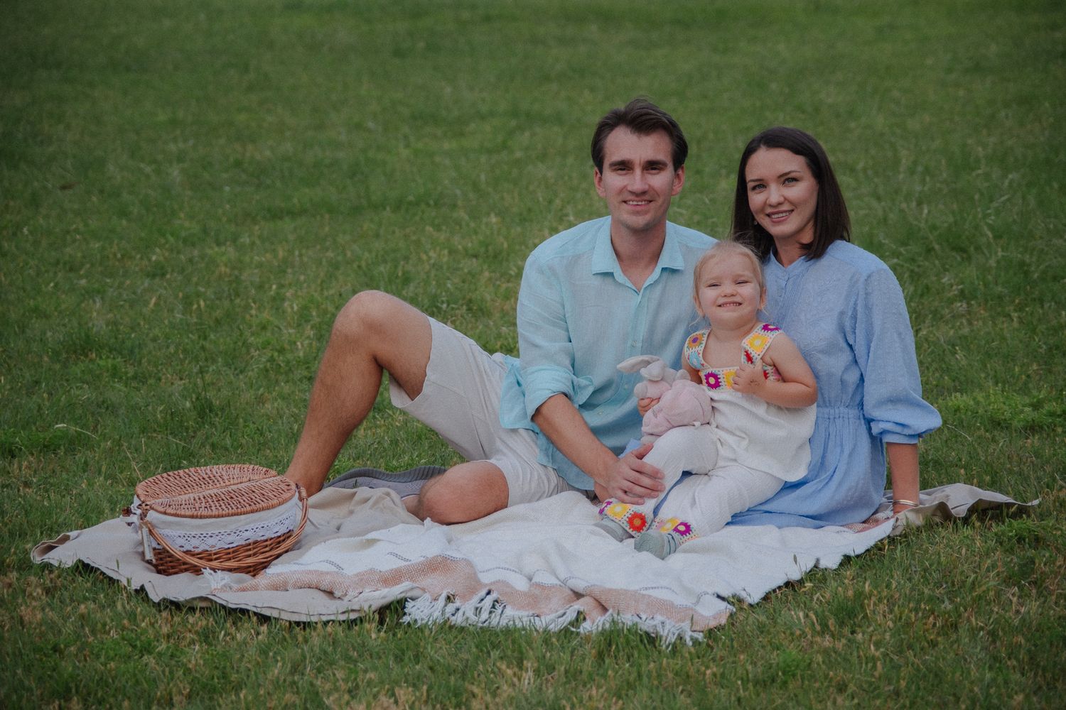 A family enjoys a summer picnic together on a blanket in a grassy field.