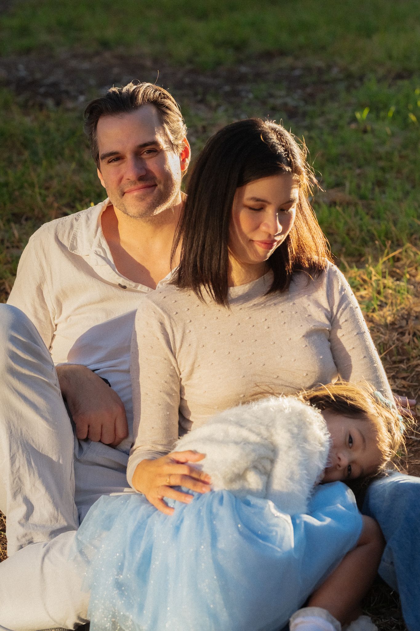 Couple in white outfits sitting together on grass during a romantic outdoor photoshoot.