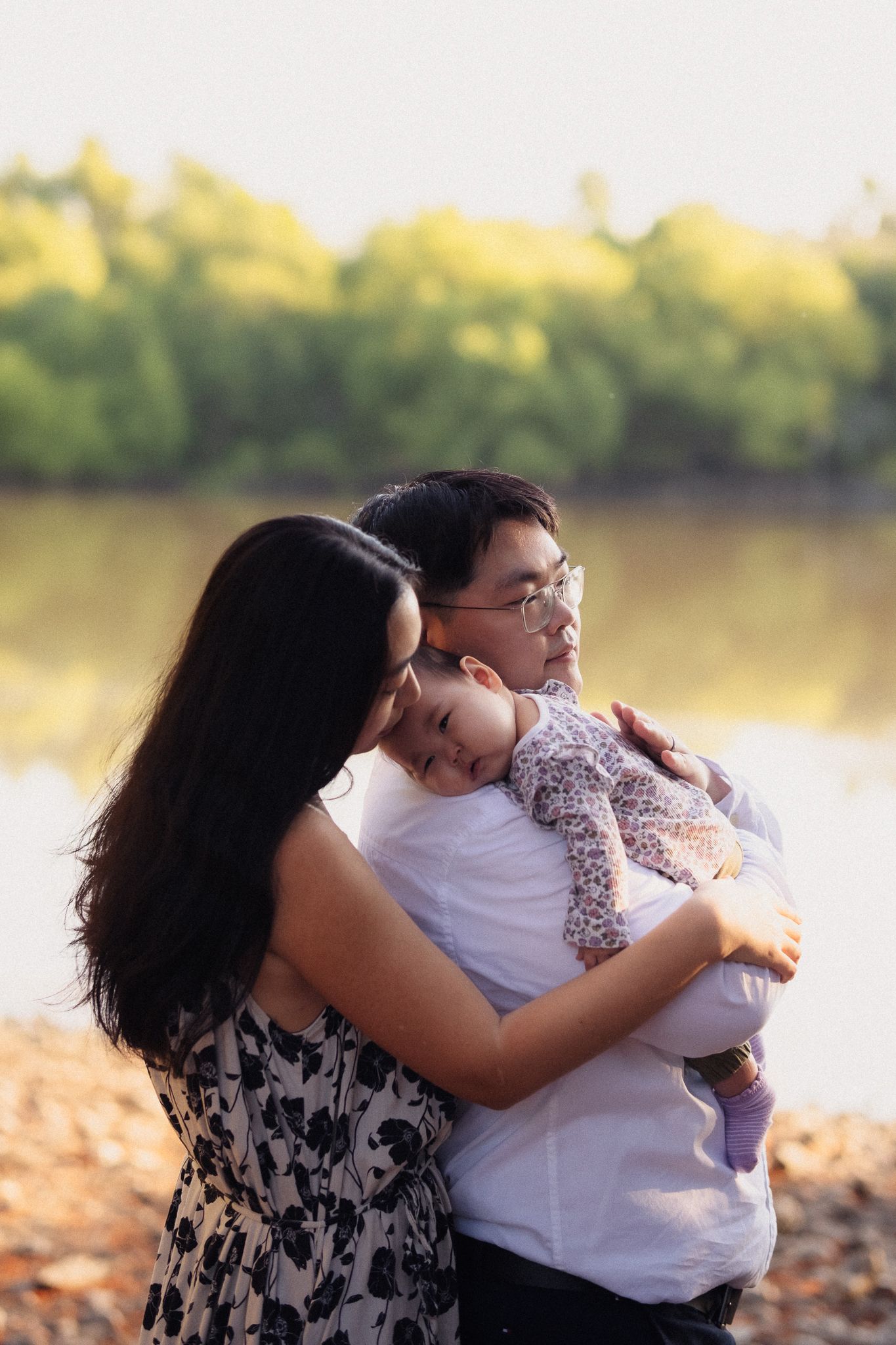 A tender family moment captured in warm sunlight by a lake as autumn leaves scatter on the ground.