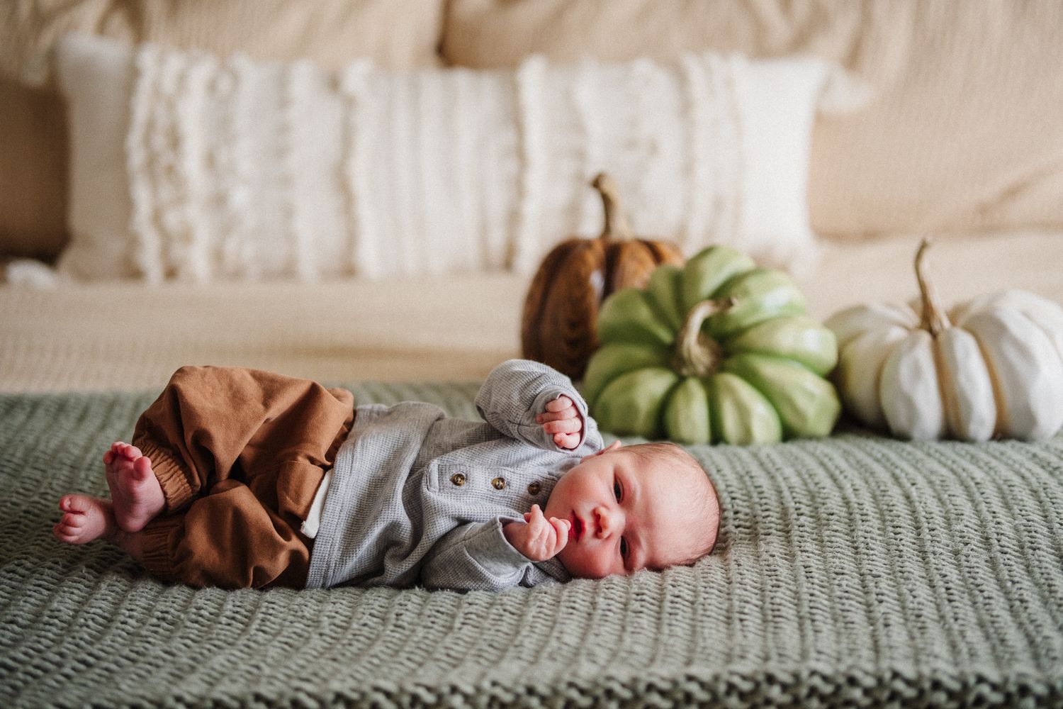 A sleeping newborn baby rests on a textured gray blanket in natural light.