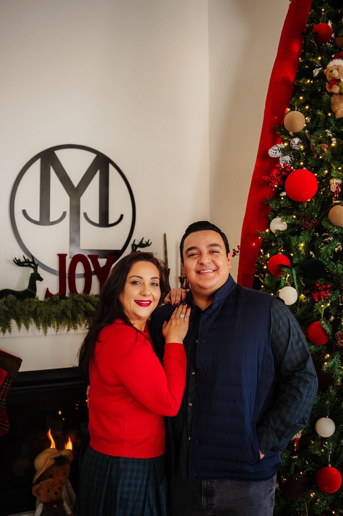 A group of people pose together in front of a decorated Christmas tree with red ornaments and white walls.