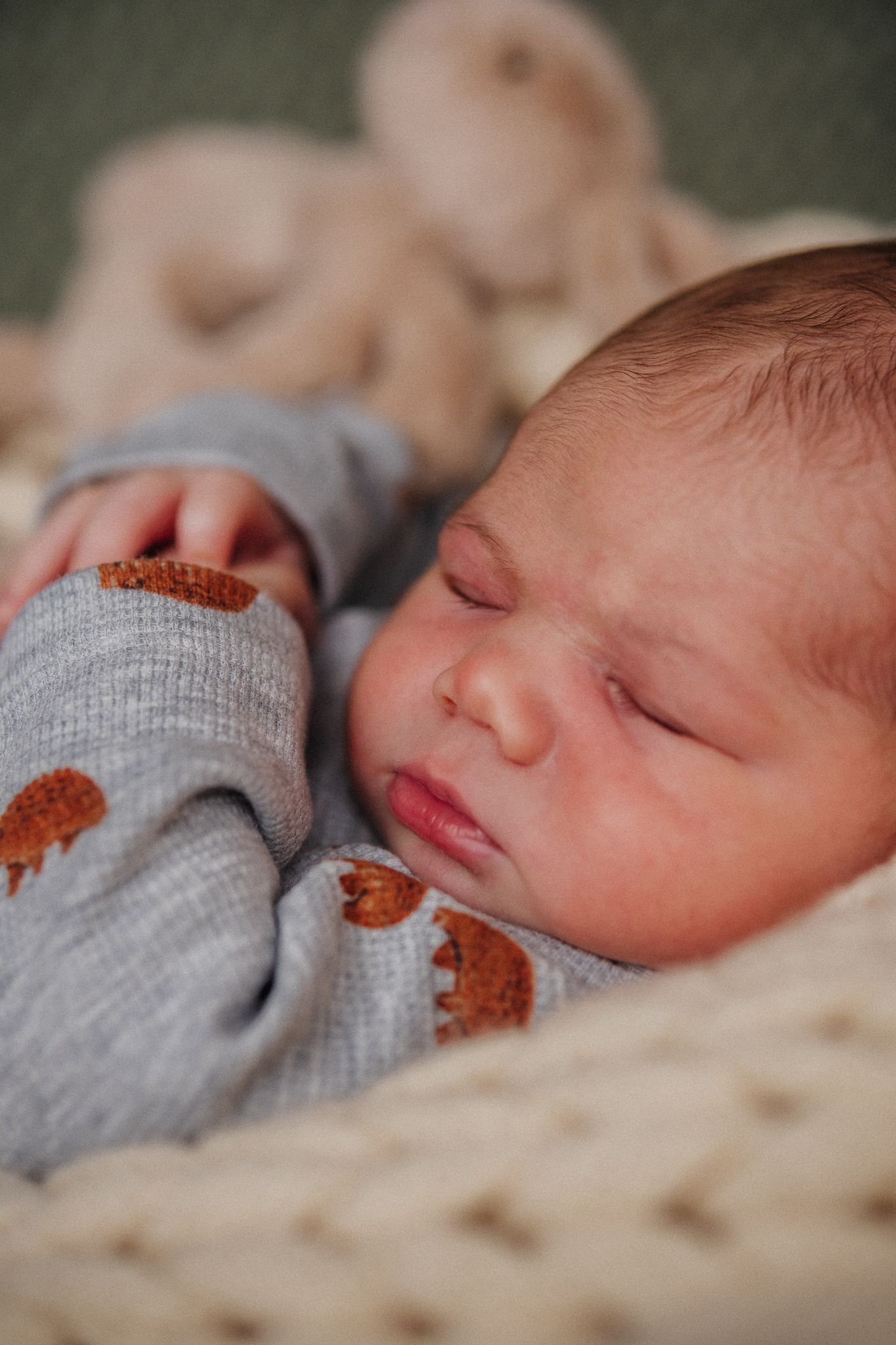 Sleeping newborn baby wearing gray clothing against textured background.