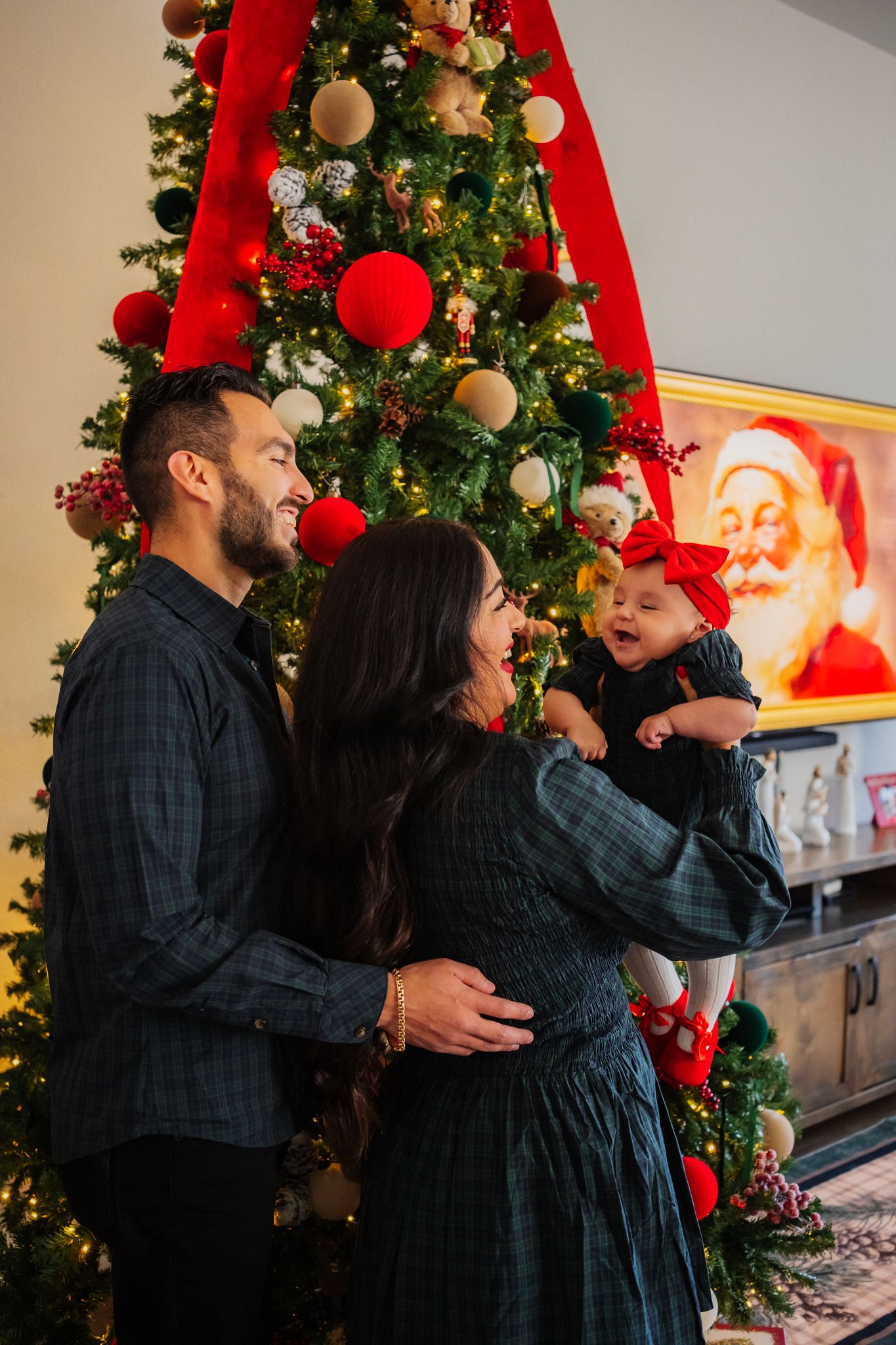 Family shares warm embraces and holiday cheer in front of a glowing Christmas tree with red ornaments.