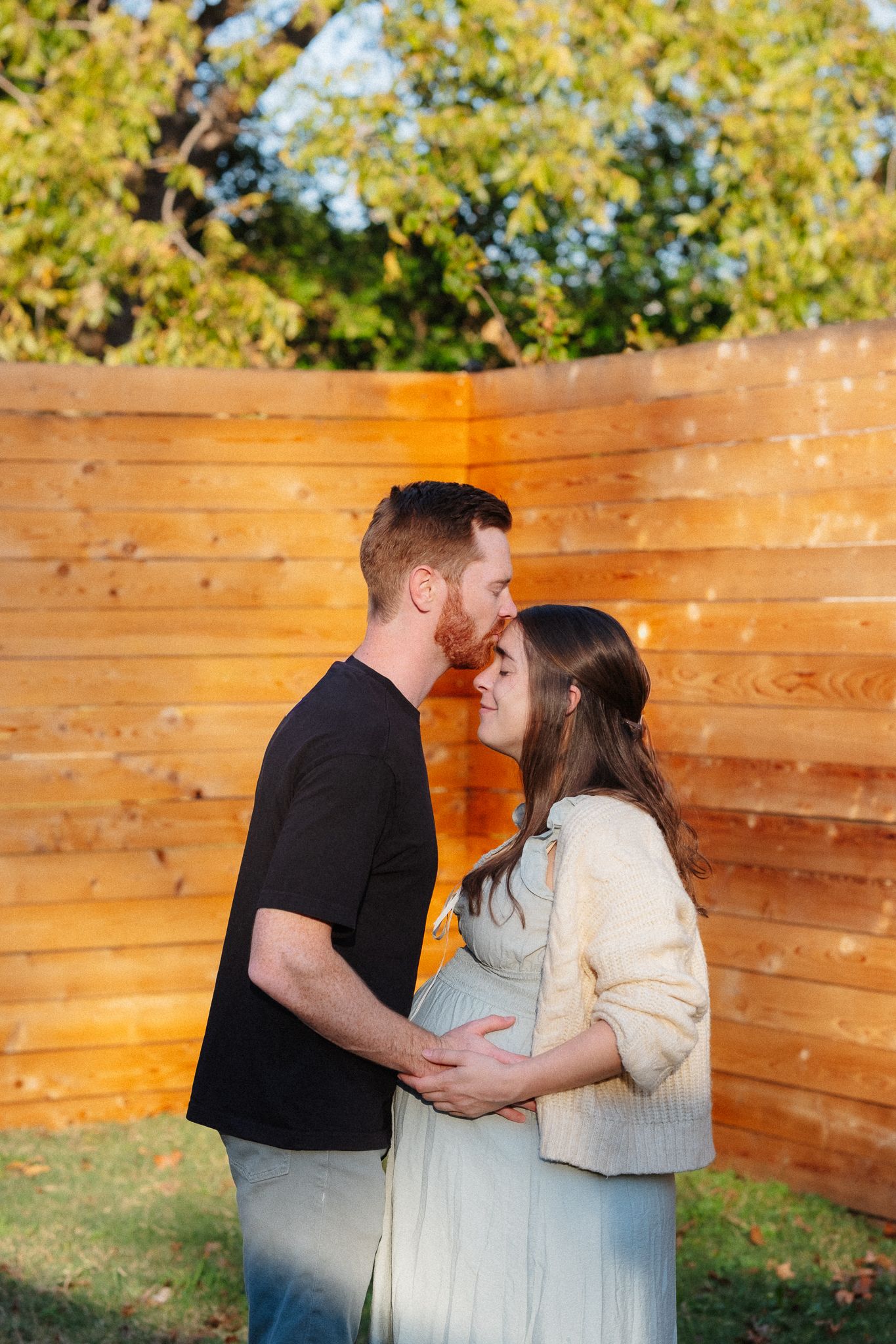 Romantic outdoor maternity session with couple embracing by wooden fence at golden hour.