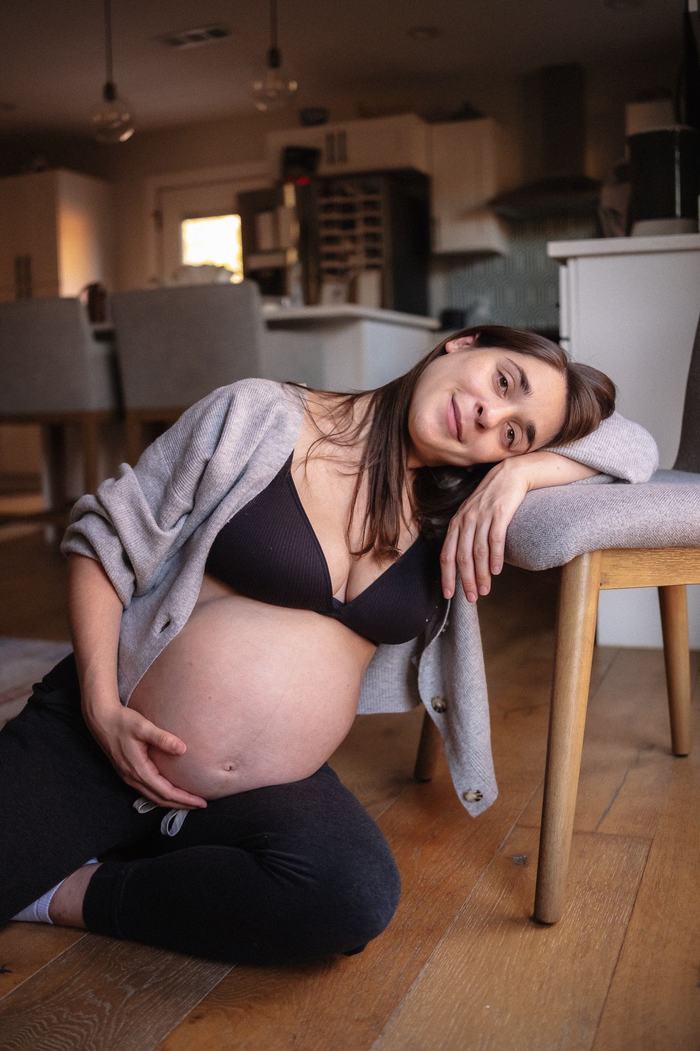 Indoor maternity boudoir session with soft natural lighting on wooden floor.