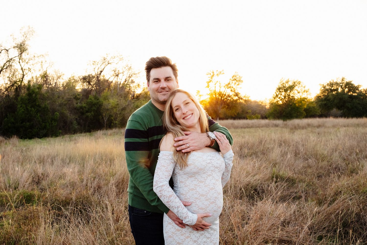 A couple embraces in a golden field during sunset creating a romantic outdoor portrait session.